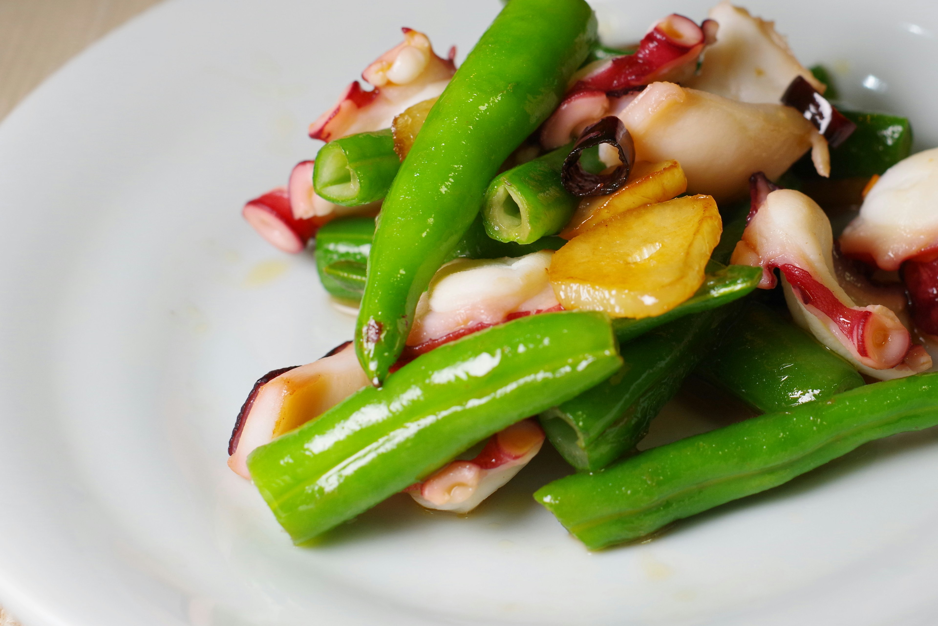 Un plato con pimientos verdes y pulpo servido en un plato blanco