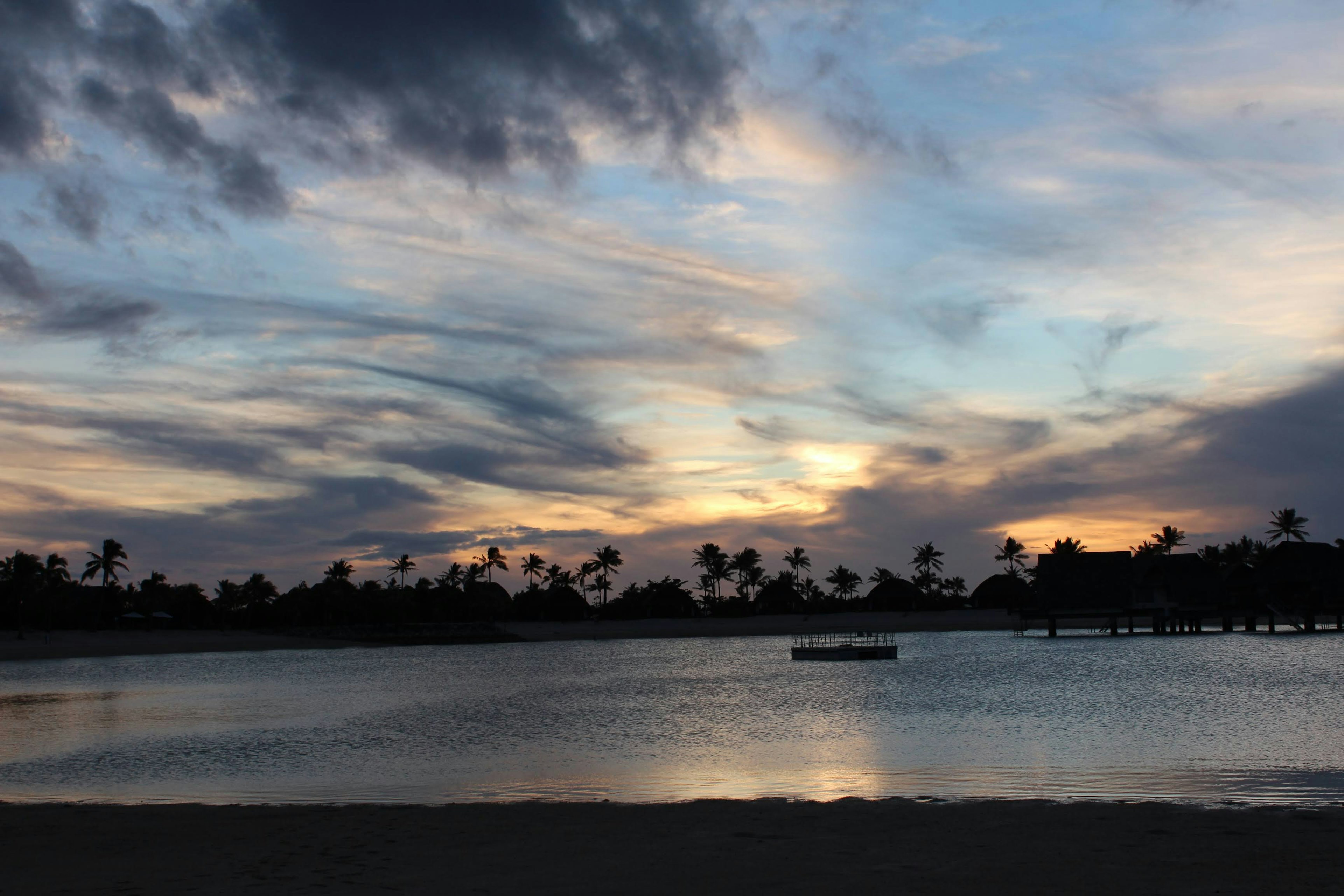 Beautiful sunset sky with tranquil water surface silhouette of palm trees along the beach