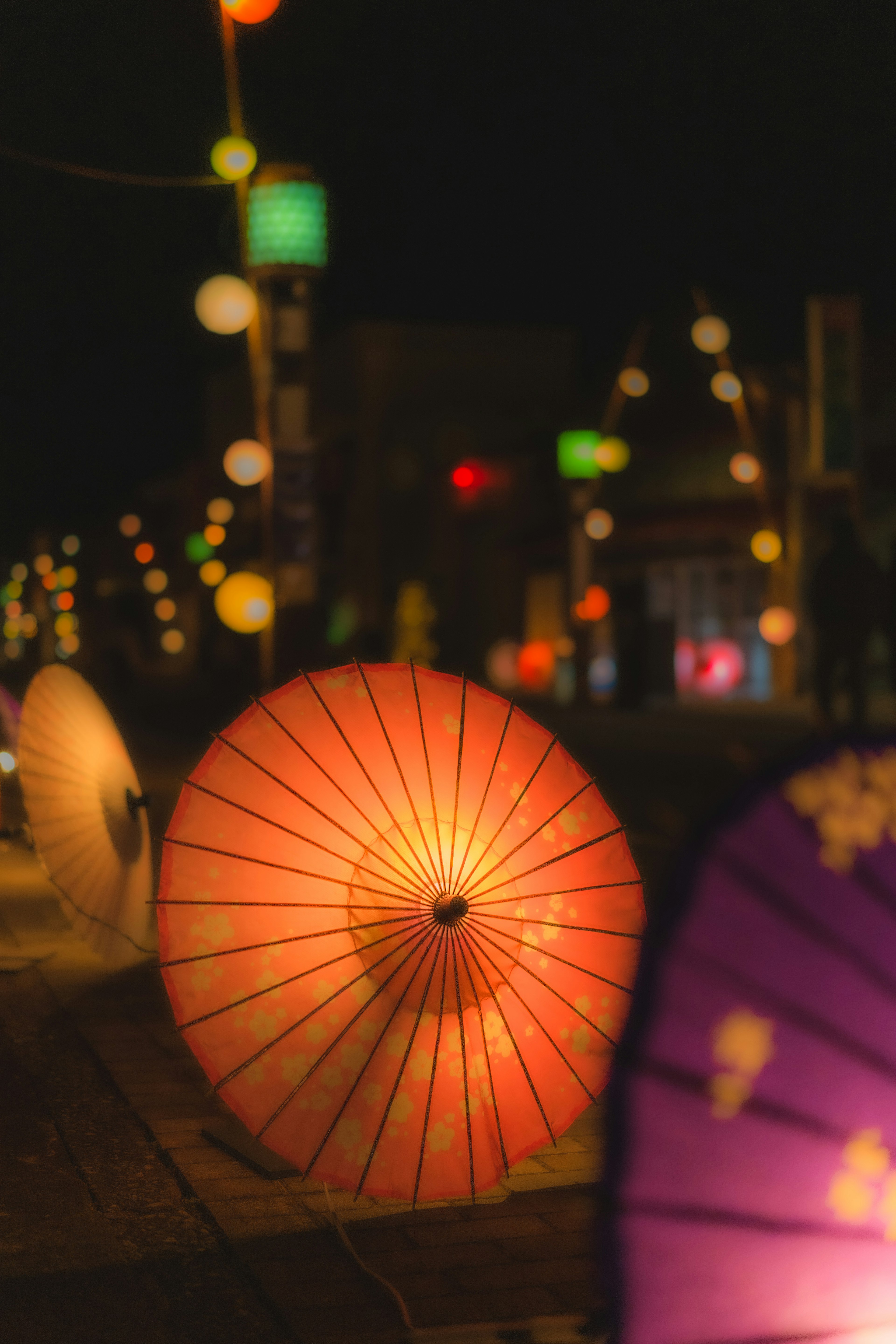 夜の街並みに並ぶカラフルな傘とランタン