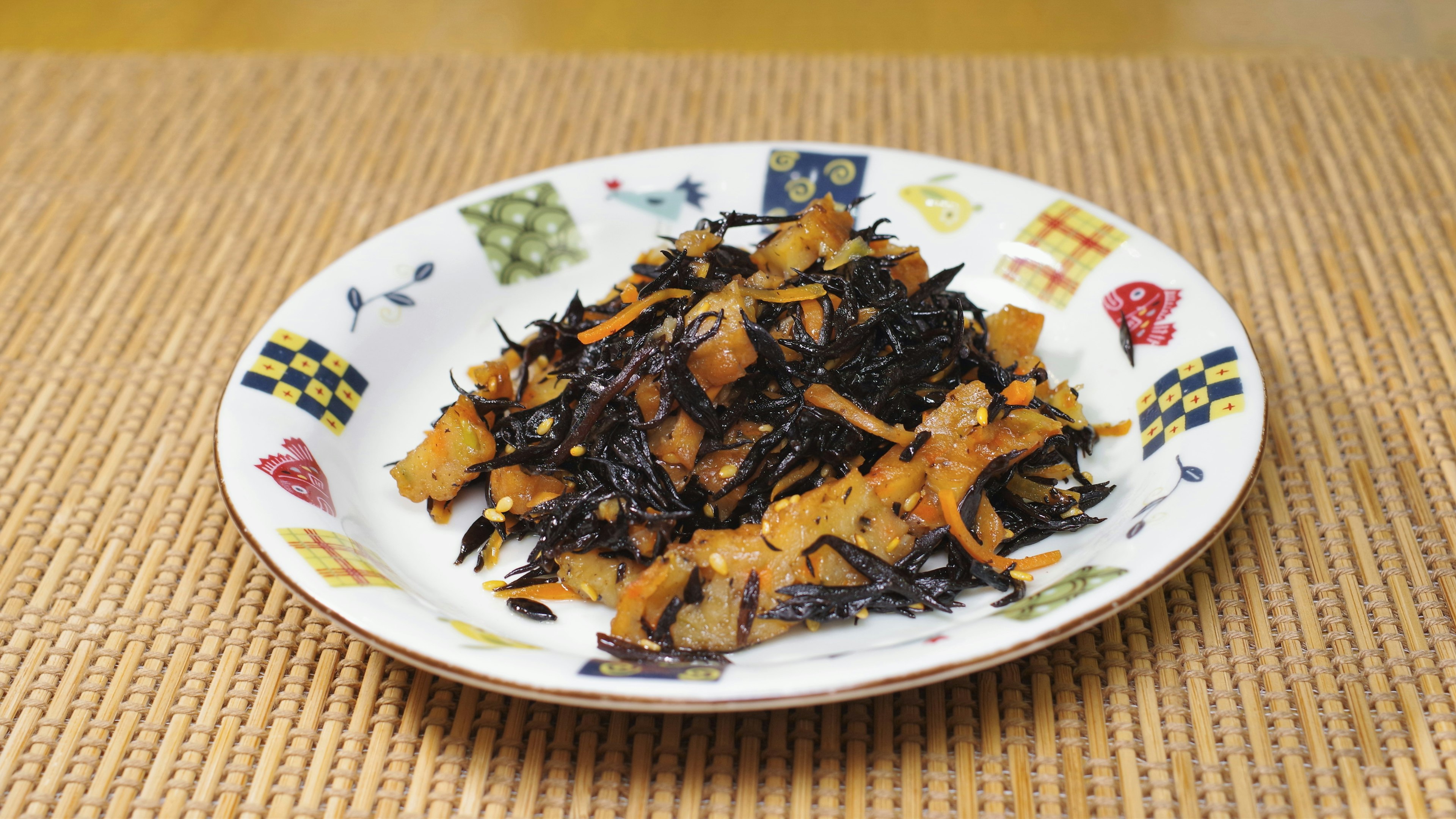 A dish of simmered hijiki seaweed and vegetables on a decorative plate