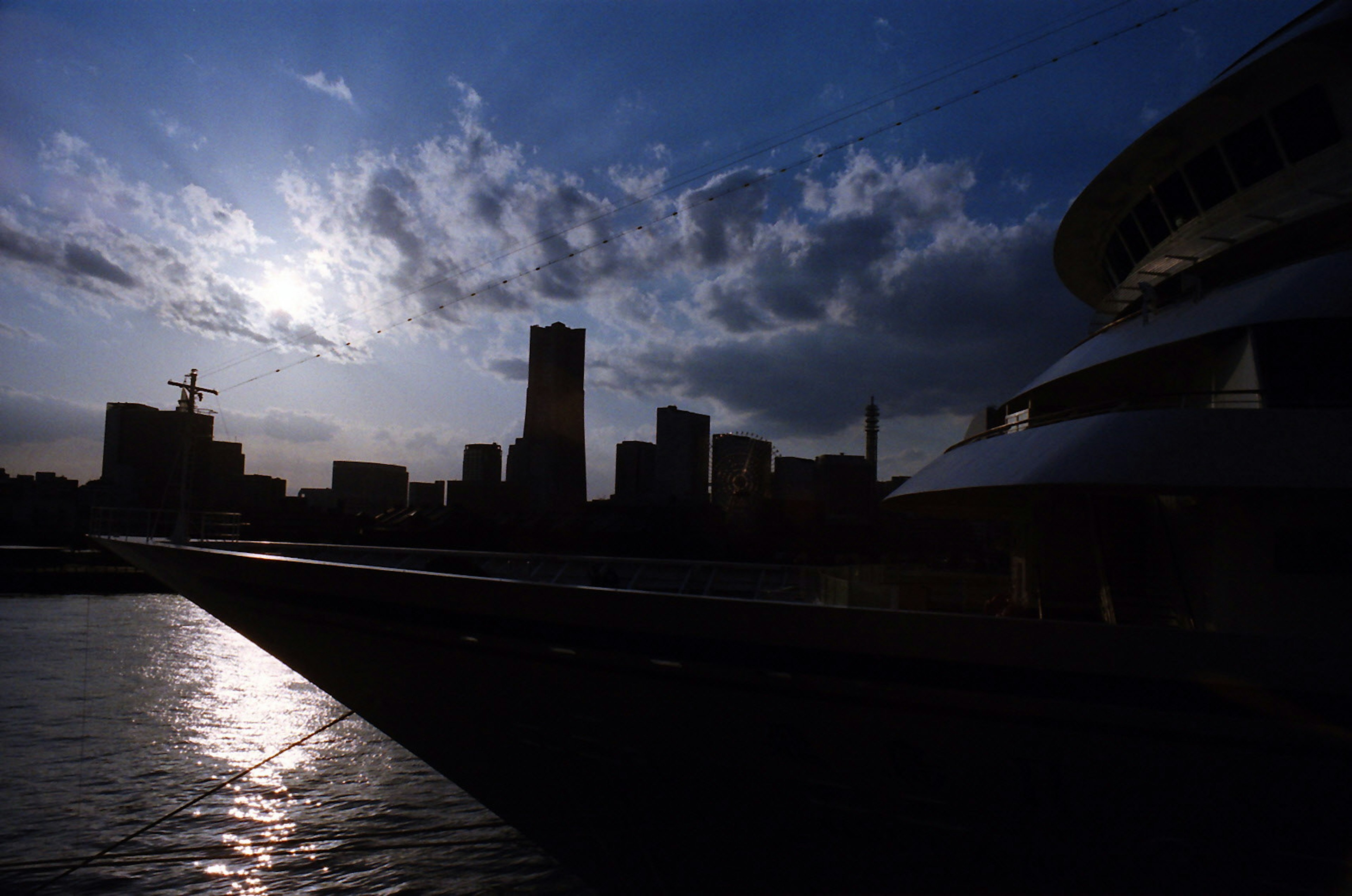 Silhouette de una ciudad al anochecer, contornos de edificios, superficie de agua tranquila, nubes dramáticas