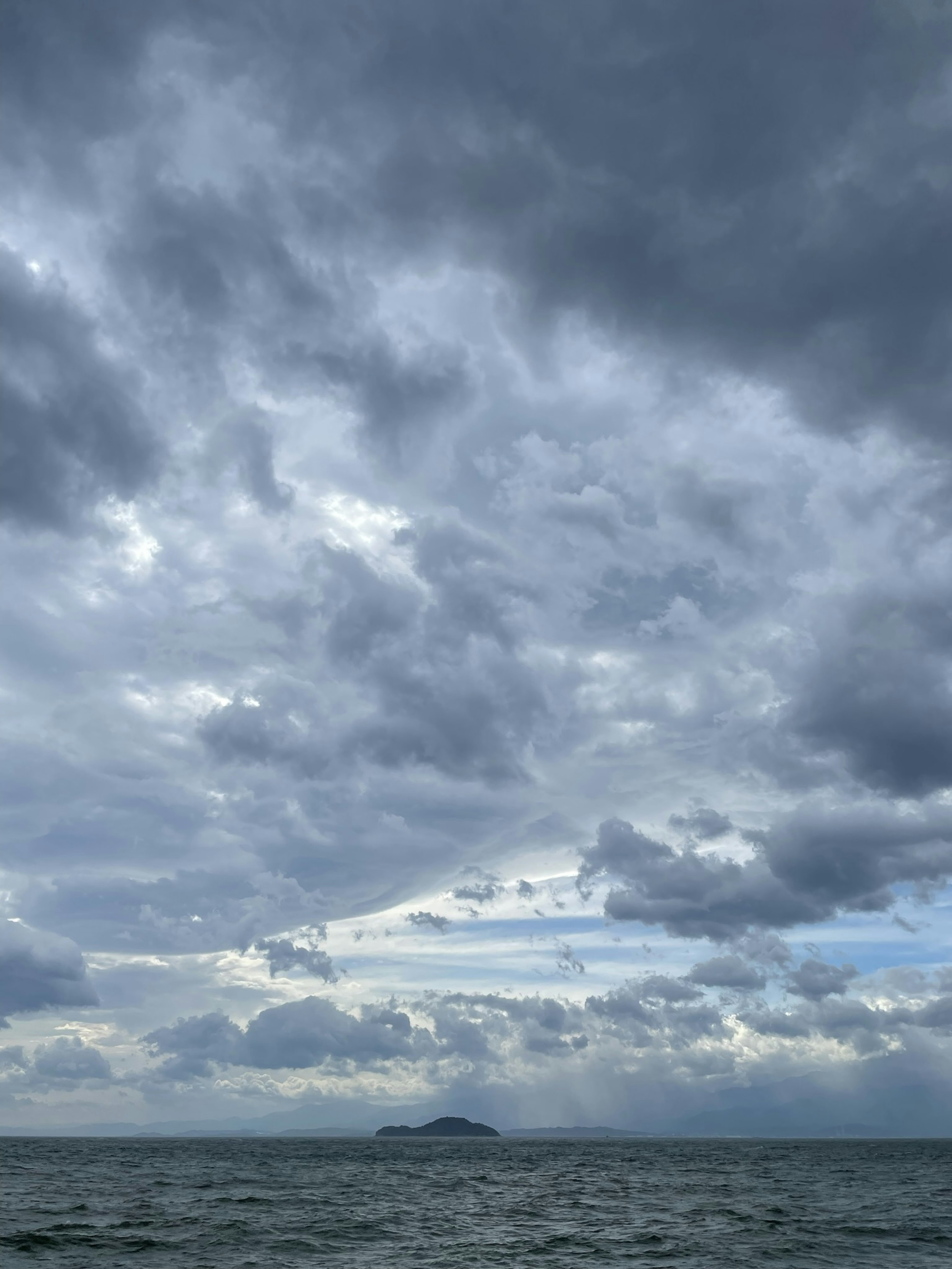 雲がたなびく海の風景に小島が浮かぶ