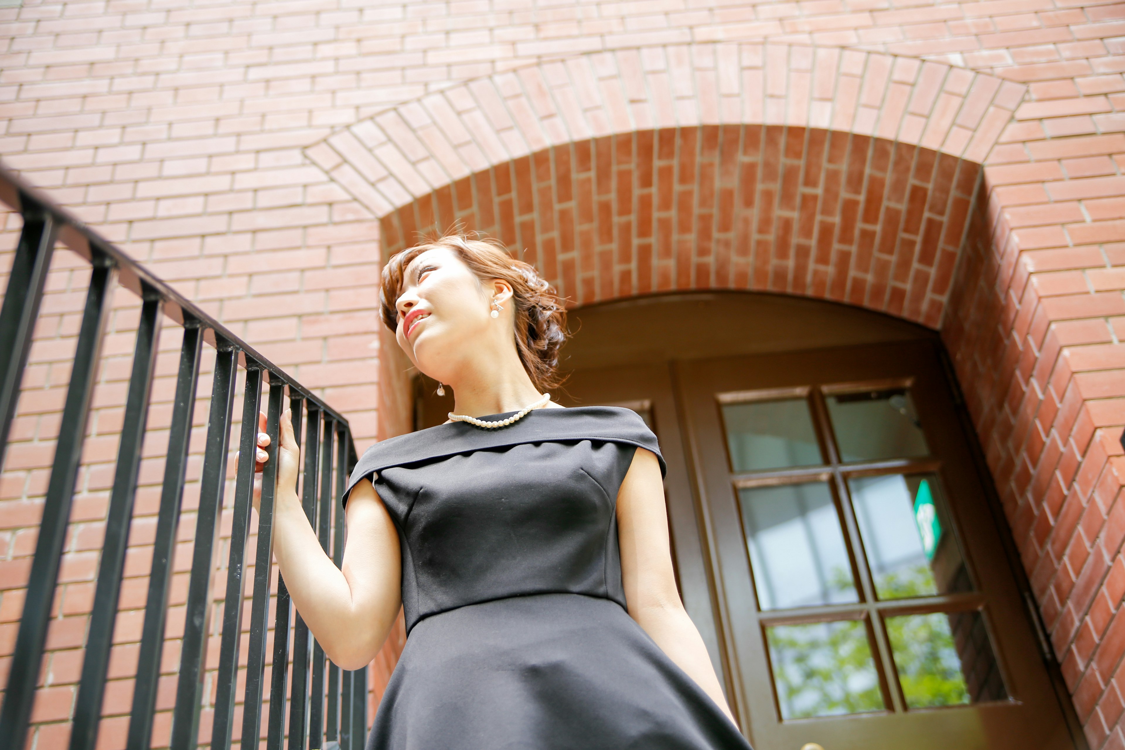 Une femme en robe noire posant devant un mur en briques