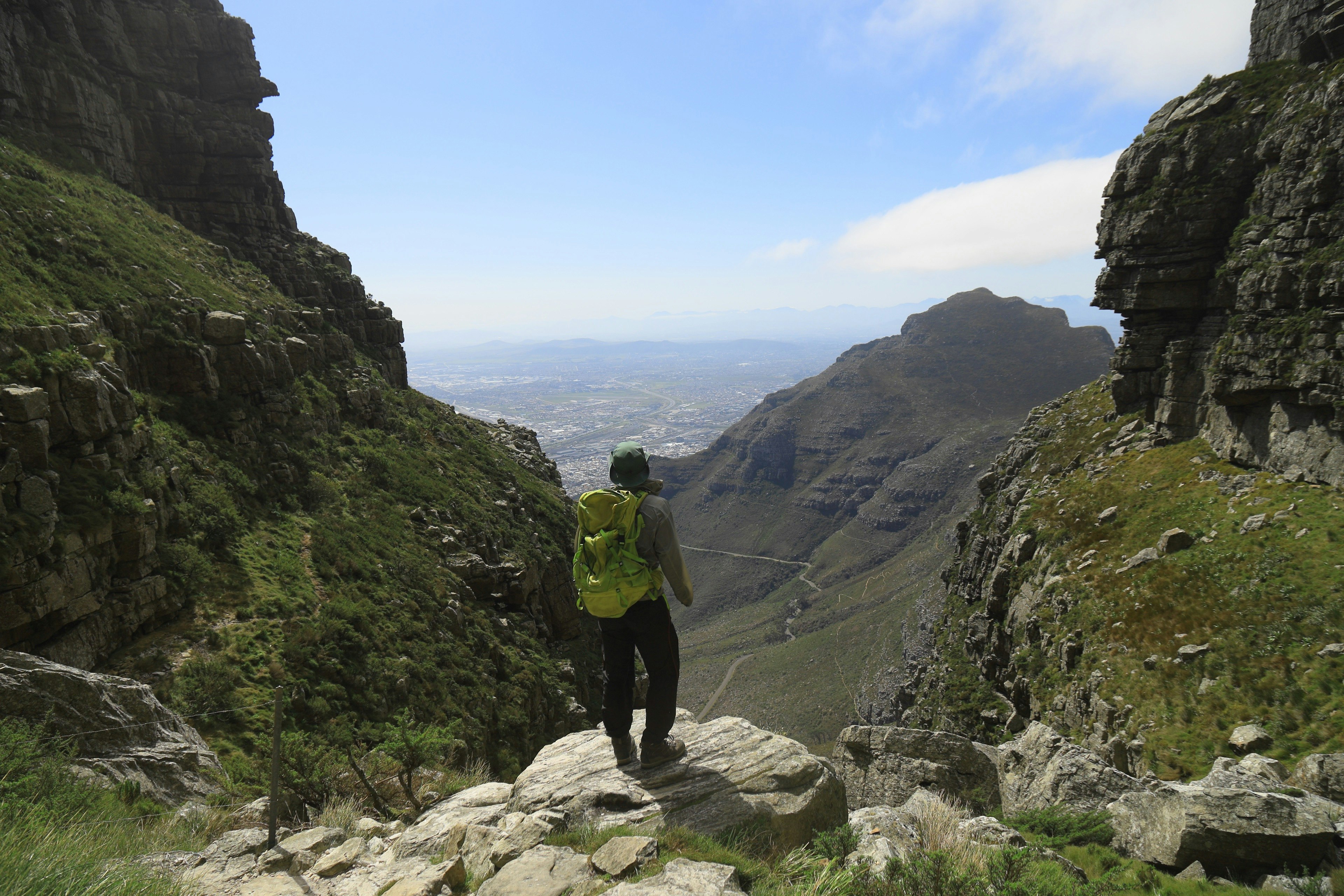 Hiker with a green backpack overlooking a stunning view from a rocky mountain path