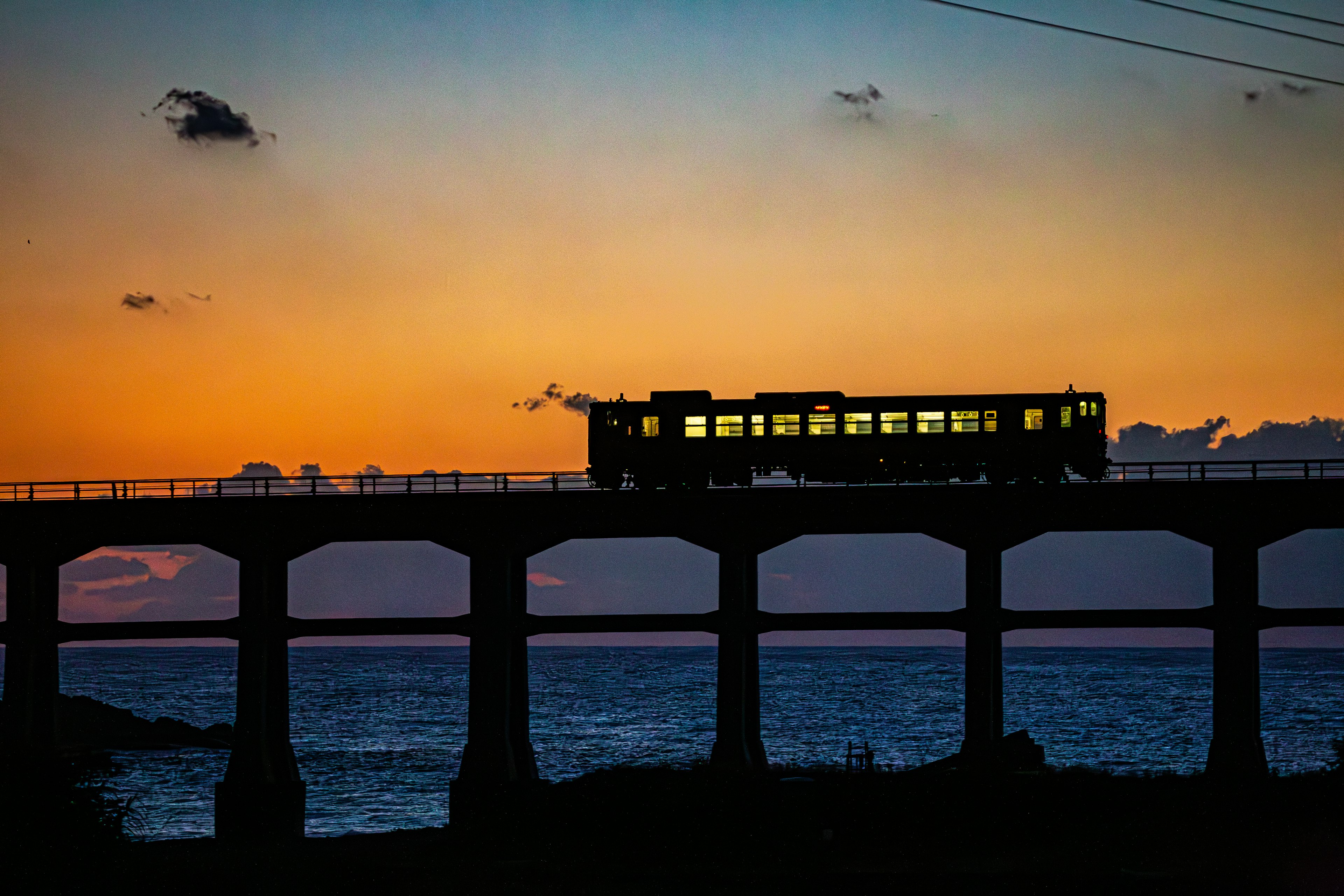 夕焼けの空を背景にした橋の上を走る電車のシルエット