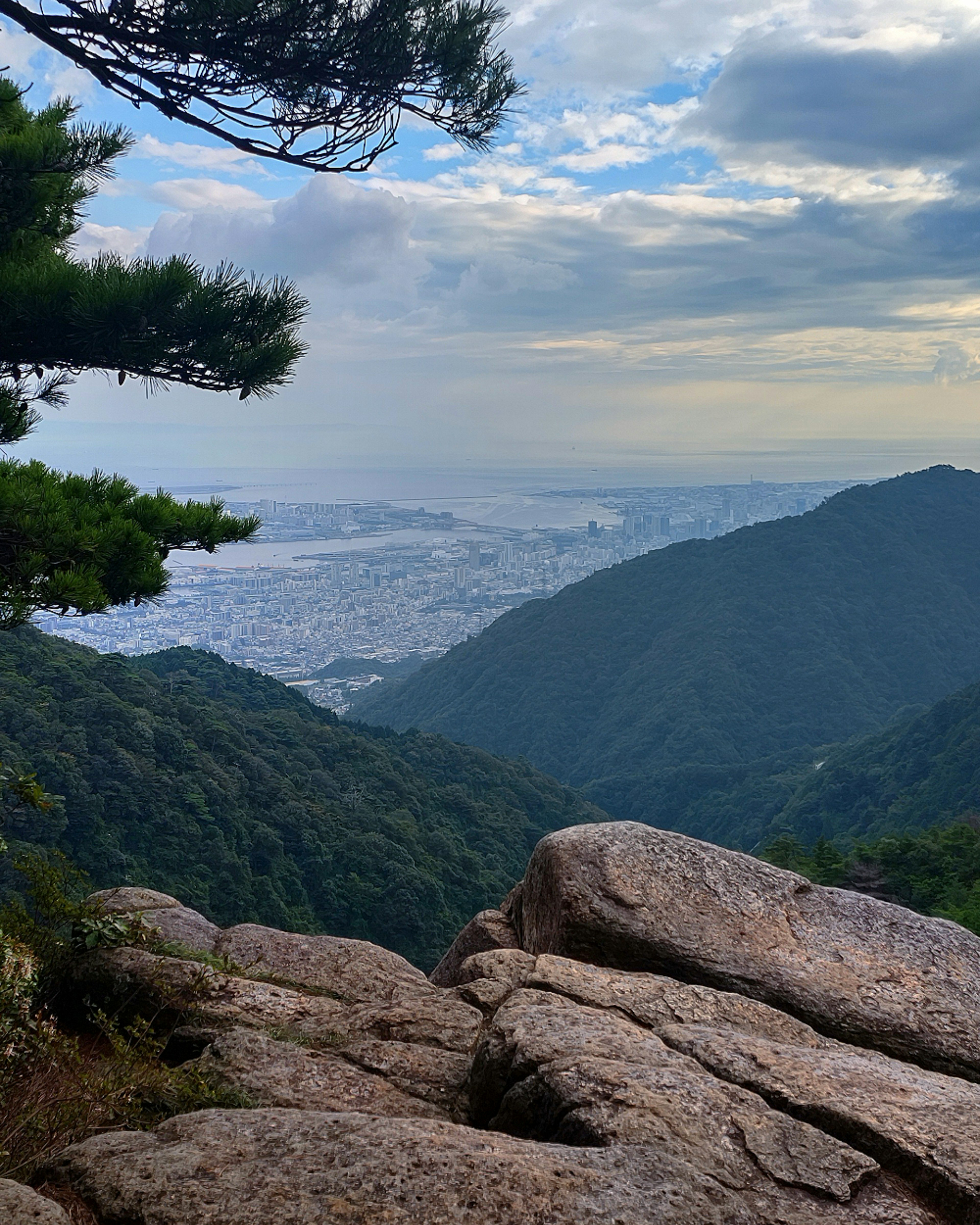 Panoramic view from a mountain peak featuring lush green hills and a distant city skyline