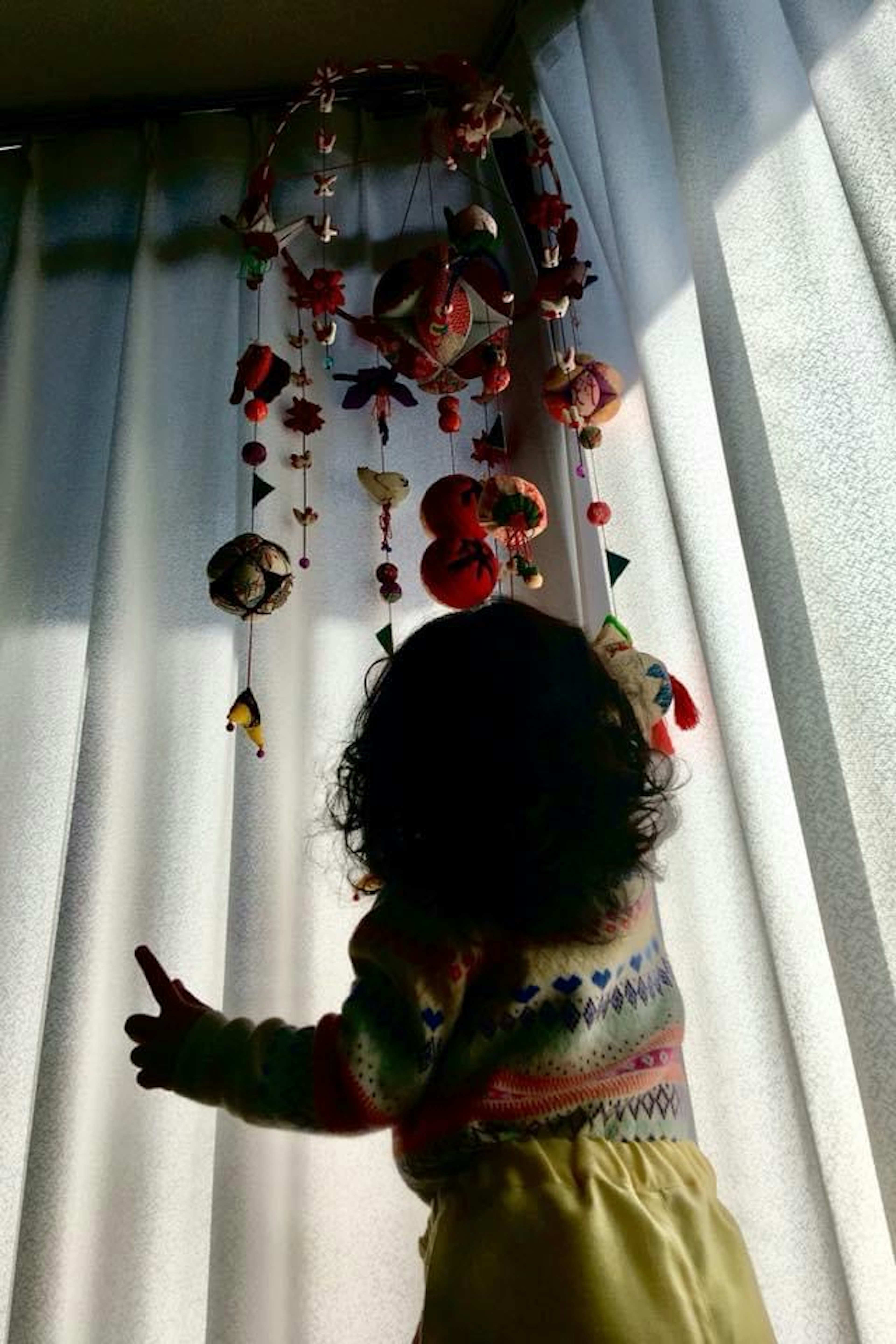 Silhouette of a child reaching for a mobile behind a curtain