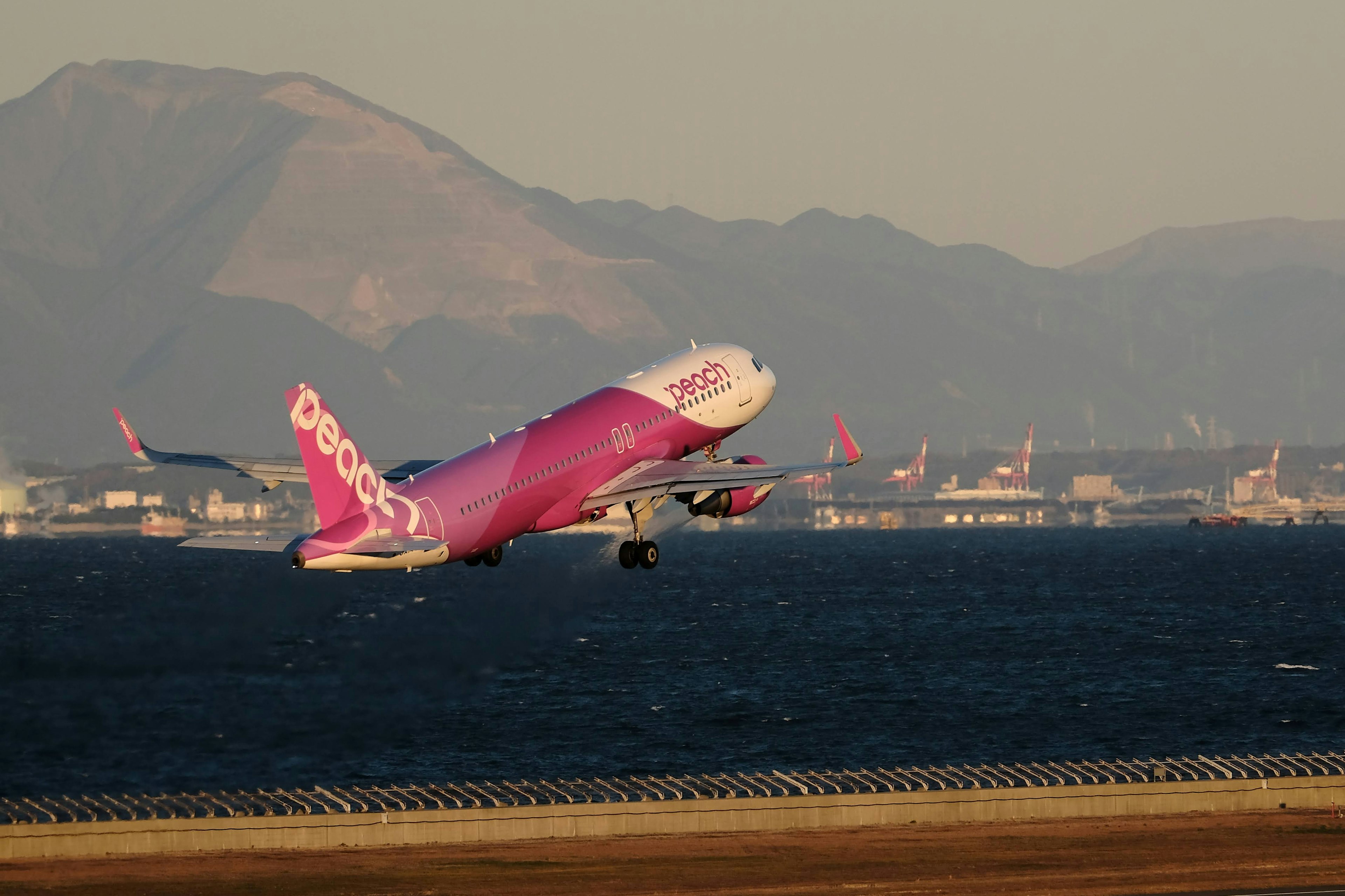 Ein rosa Flugzeug, das mit Bergen im Hintergrund abhebt