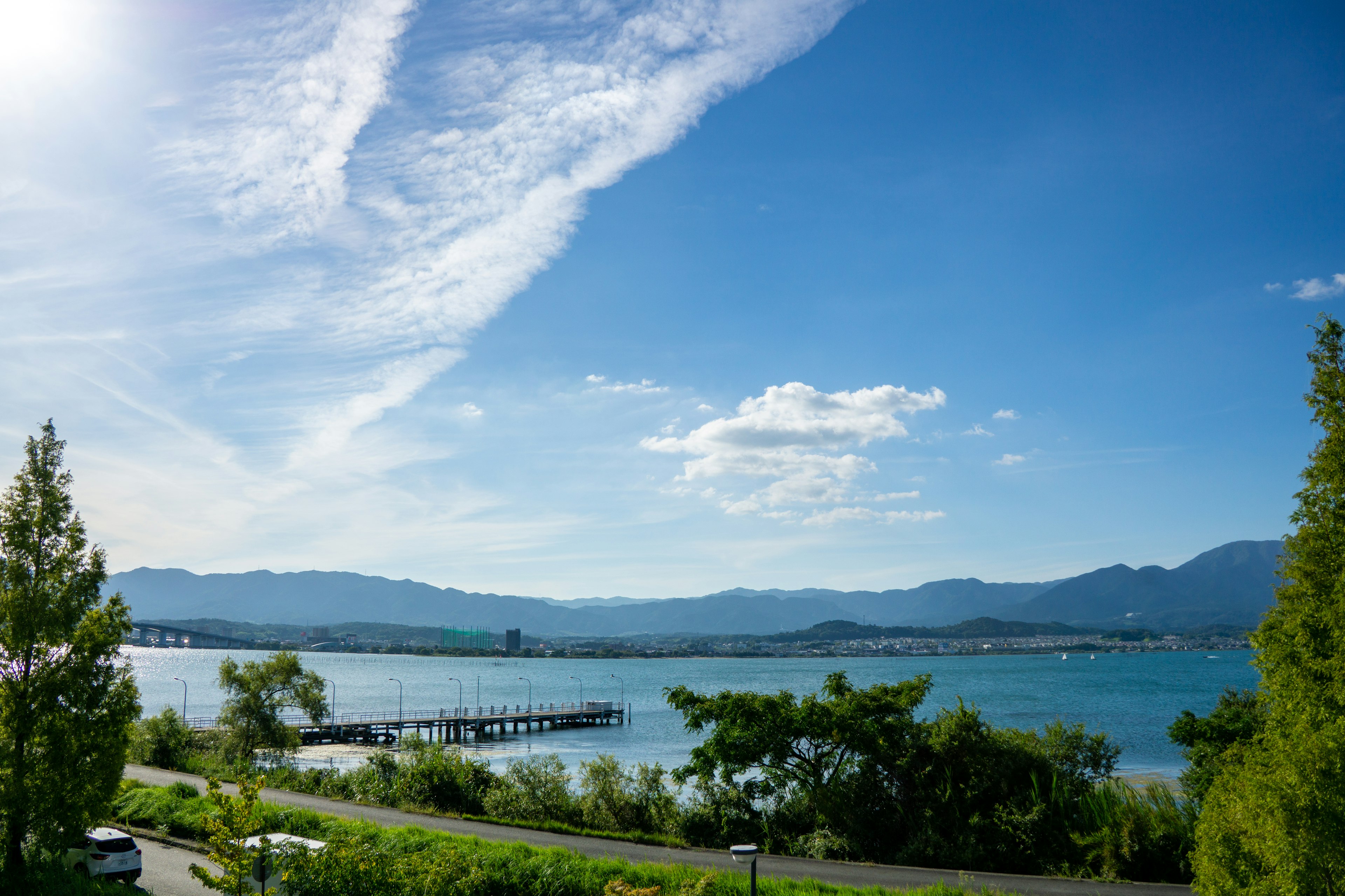 Scenic view of a lake under a blue sky with white clouds featuring green trees and a dock