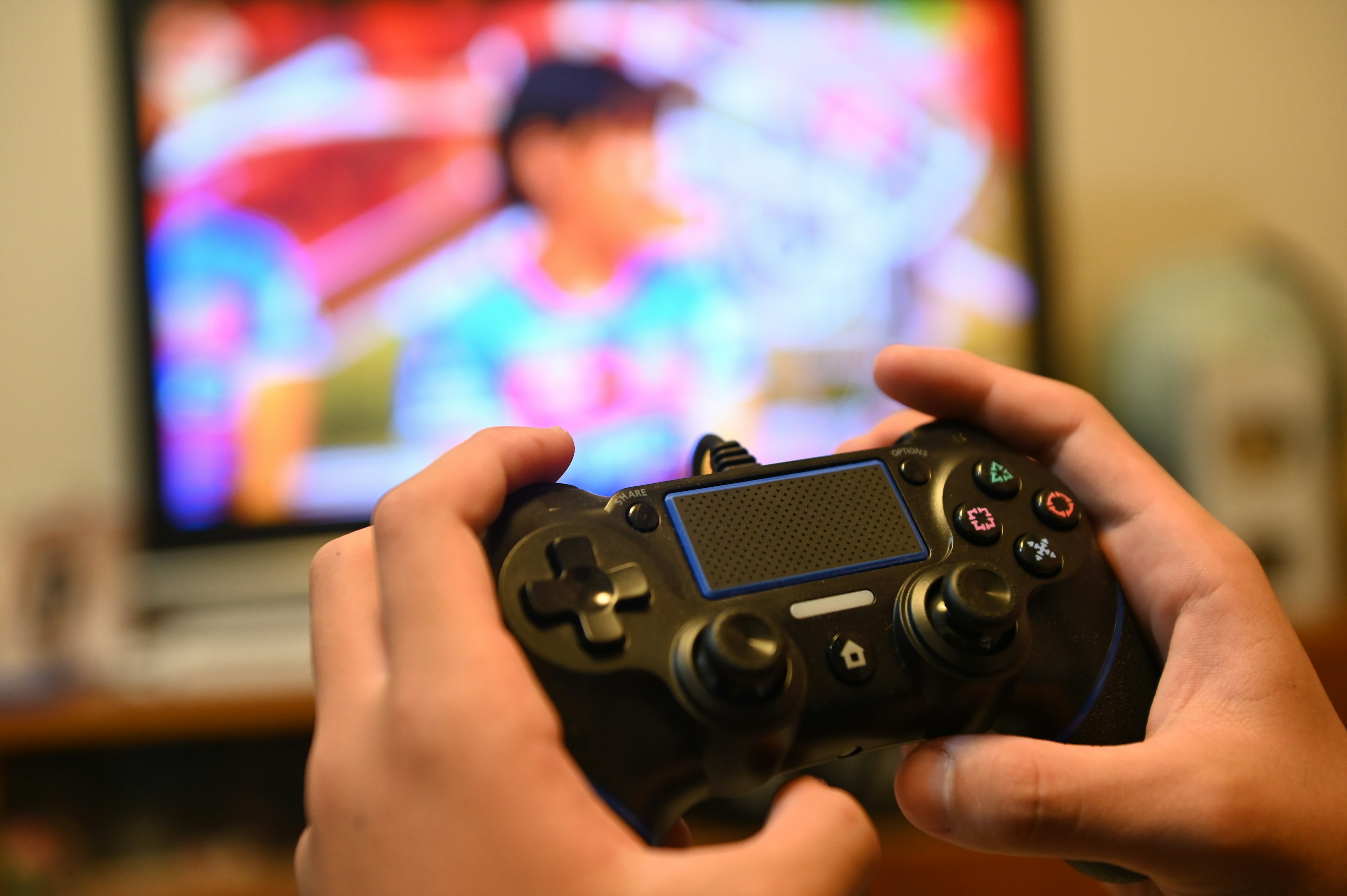 Hands holding a game controller with a colorful TV screen in the background