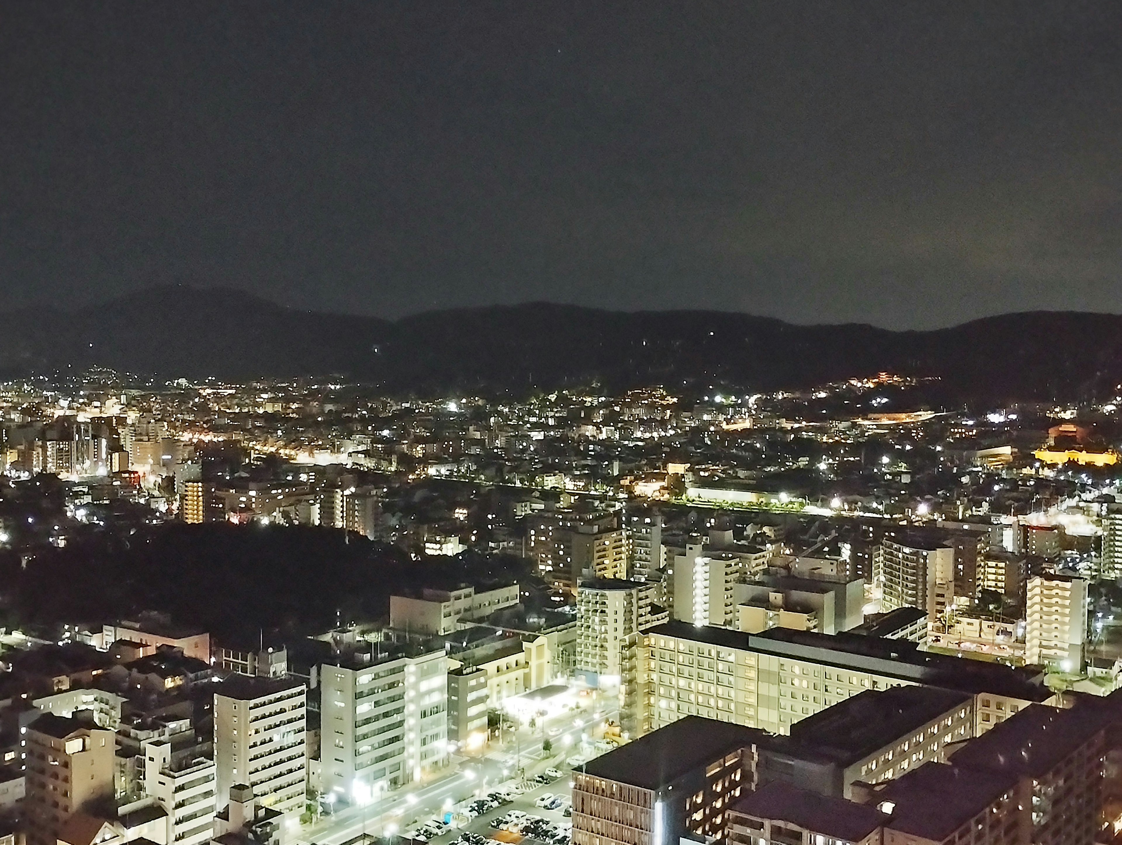 Panoramic city view at night with illuminated buildings and distant mountains