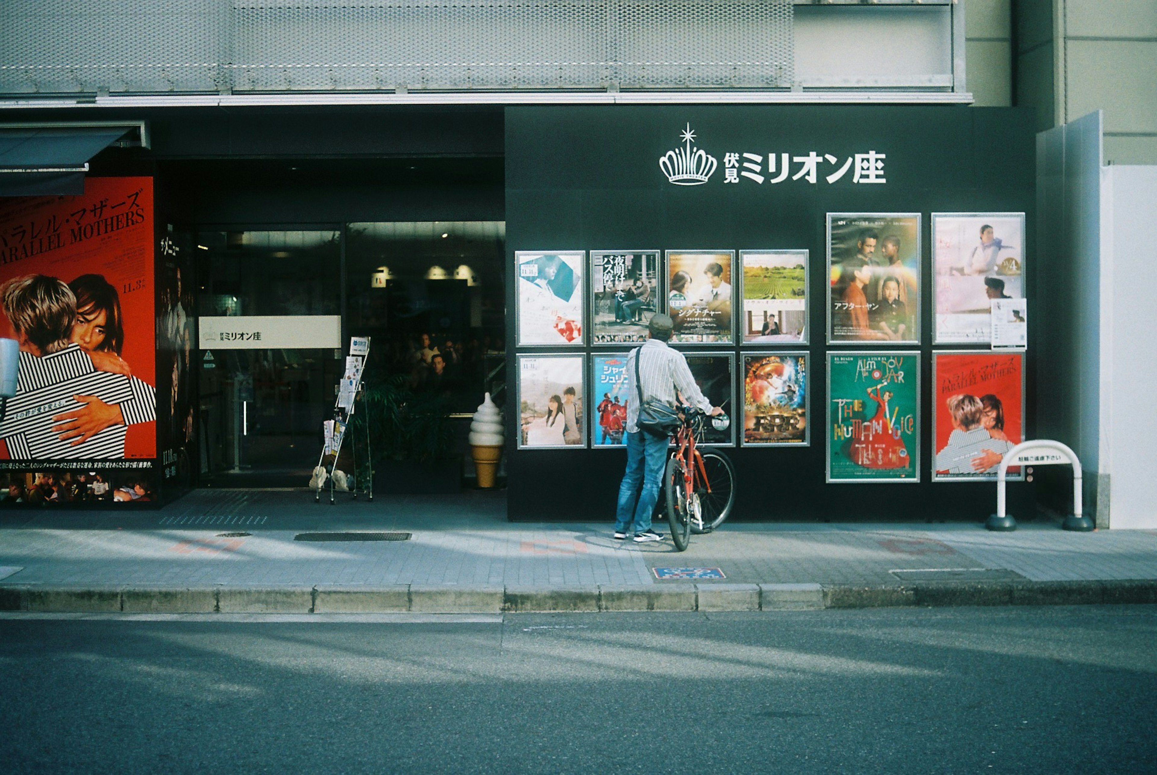 自転車に乗った男性が店舗の前を通り過ぎる画像 様々なポスターが展示されている