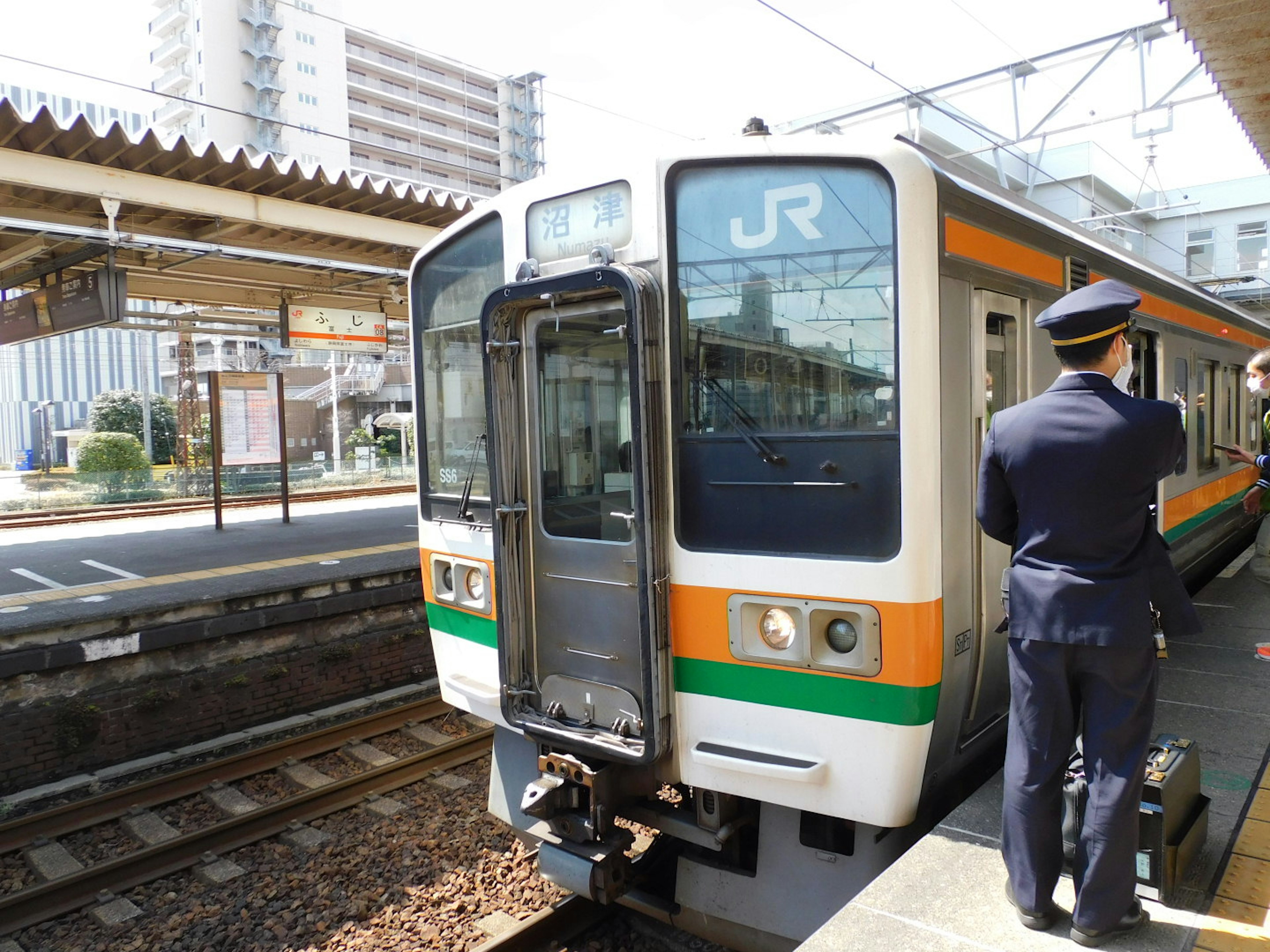 Tren JR estacionado en una estación con un empleado de estación de pie