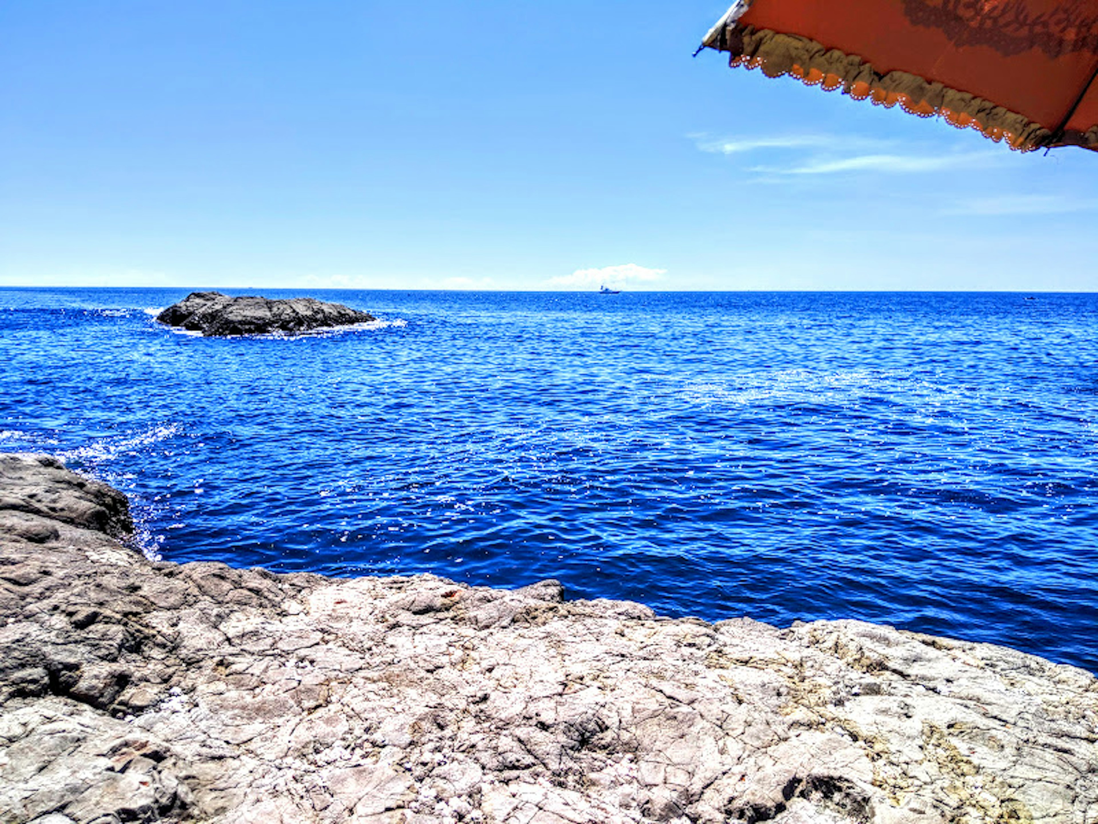 Vista panoramica dell'oceano blu e della costa rocciosa con un ombrellone