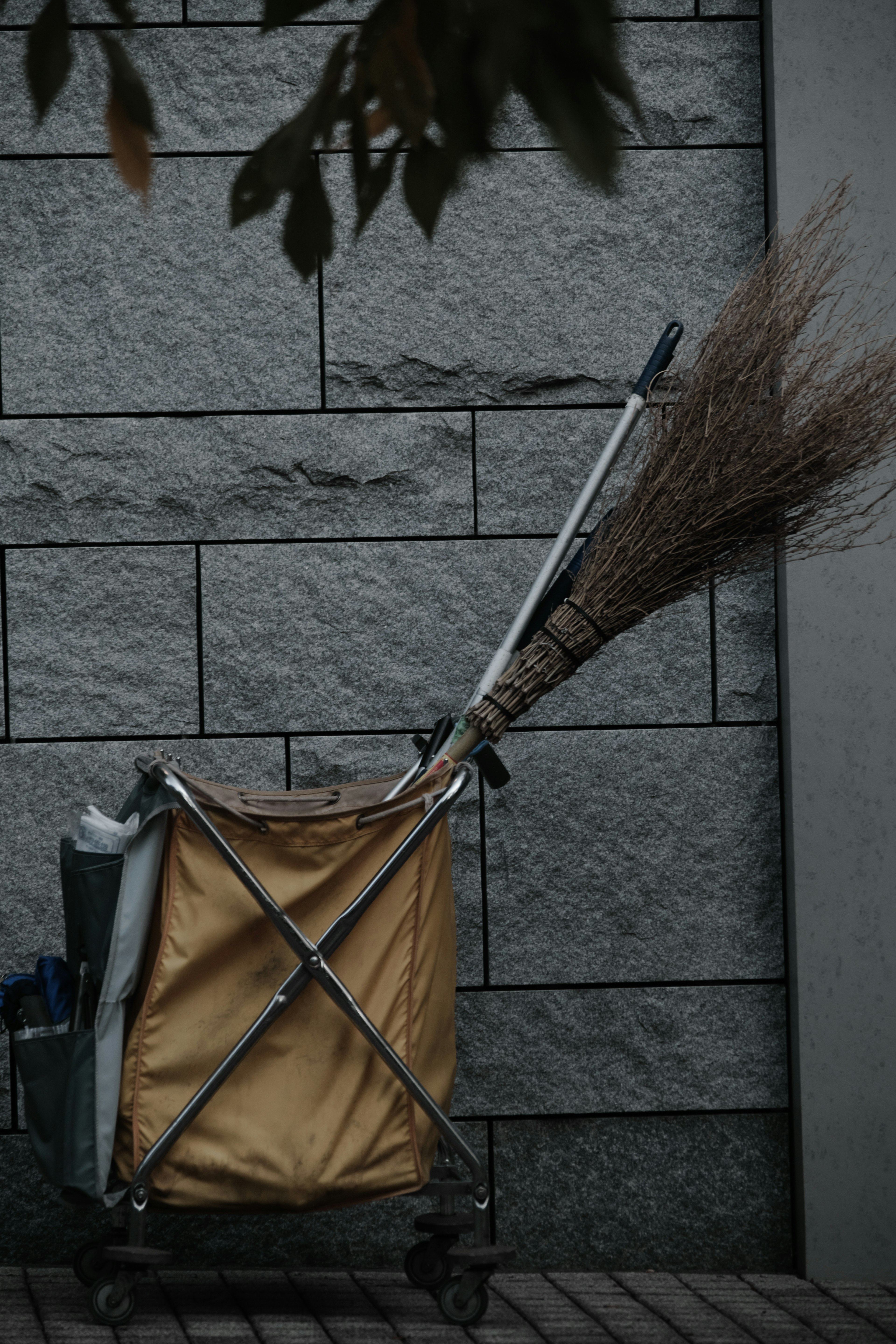 A broom leaning against a yellow cart with a stone wall