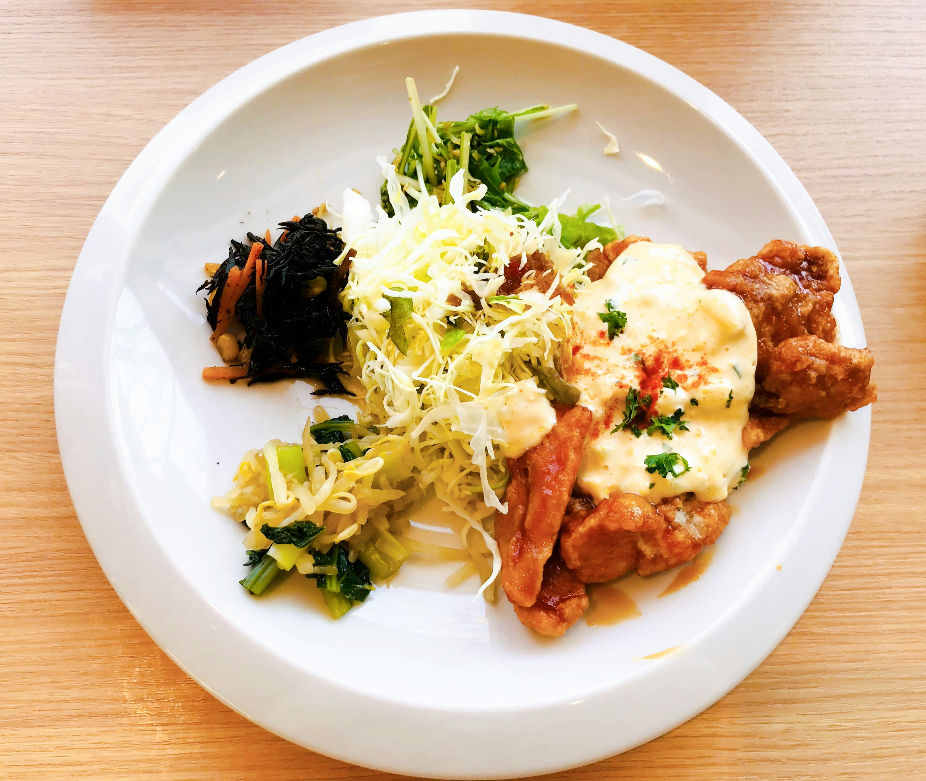 A white plate featuring fried chicken with creamy sauce shredded cabbage hijiki and assorted vegetables