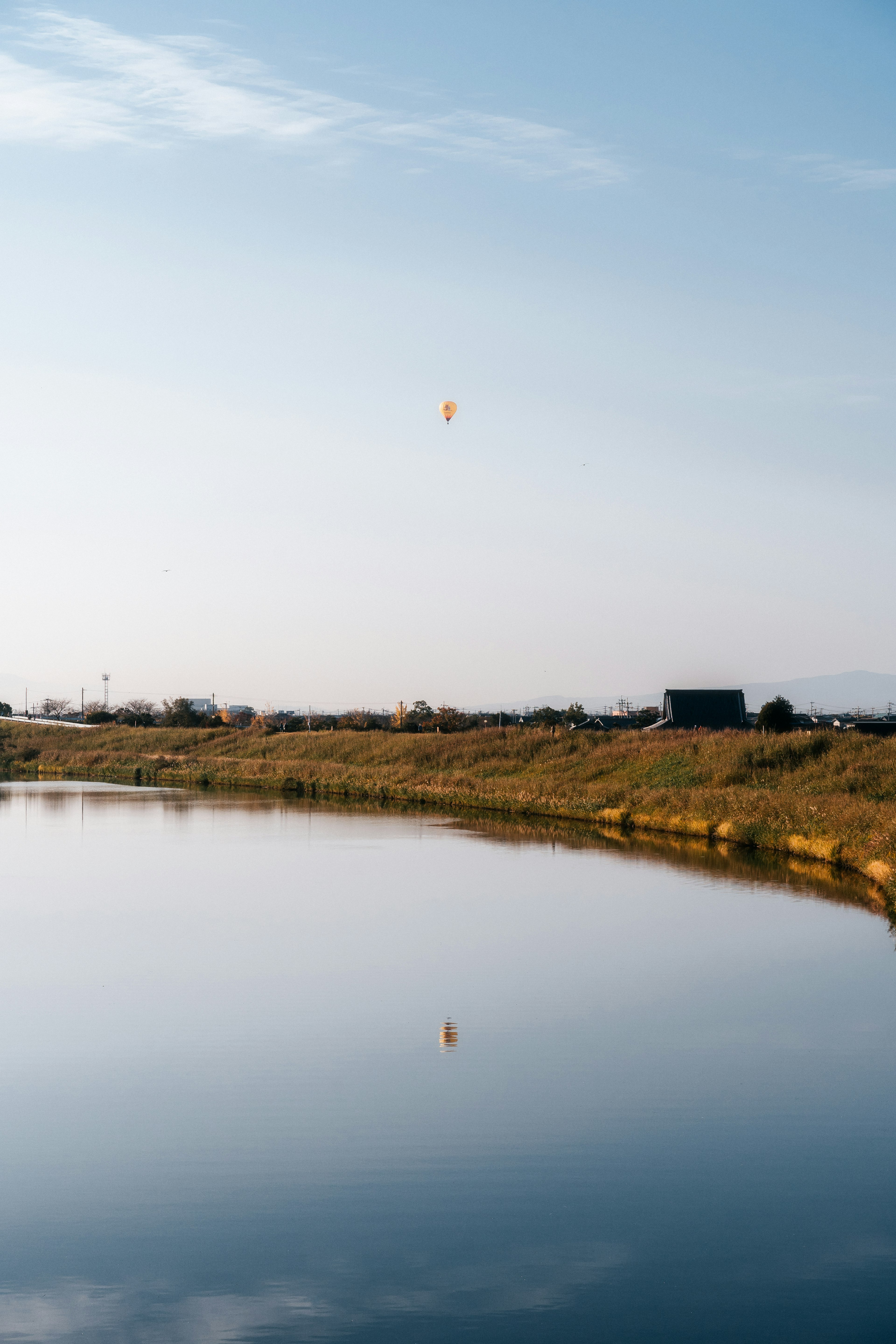 Lanskap permukaan air yang tenang dengan balon melayang di bawah langit biru dan awan yang memantulkan keindahan alam