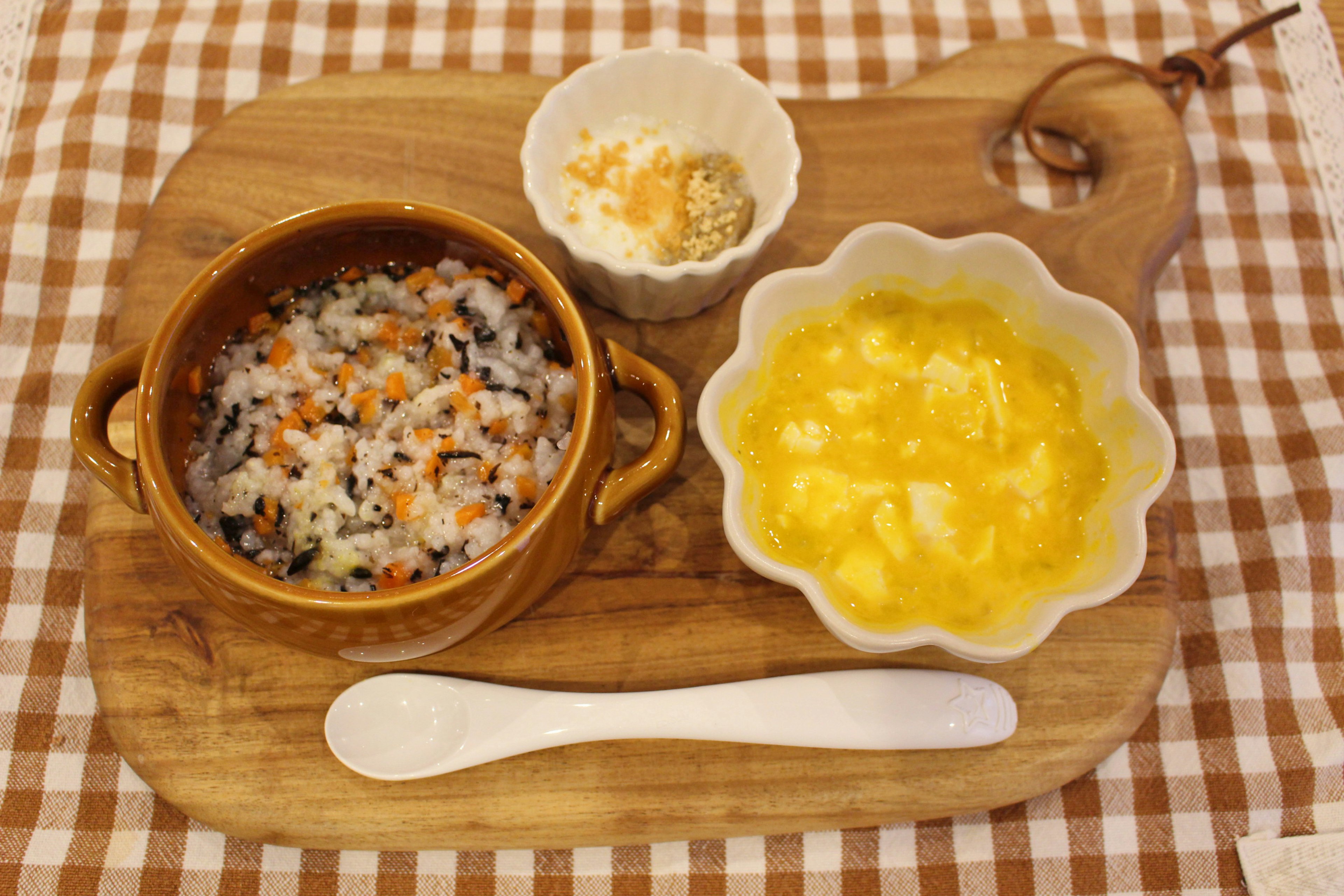 A wooden plate features Japanese-style dishes including colorful rice, egg dish, and white side dish