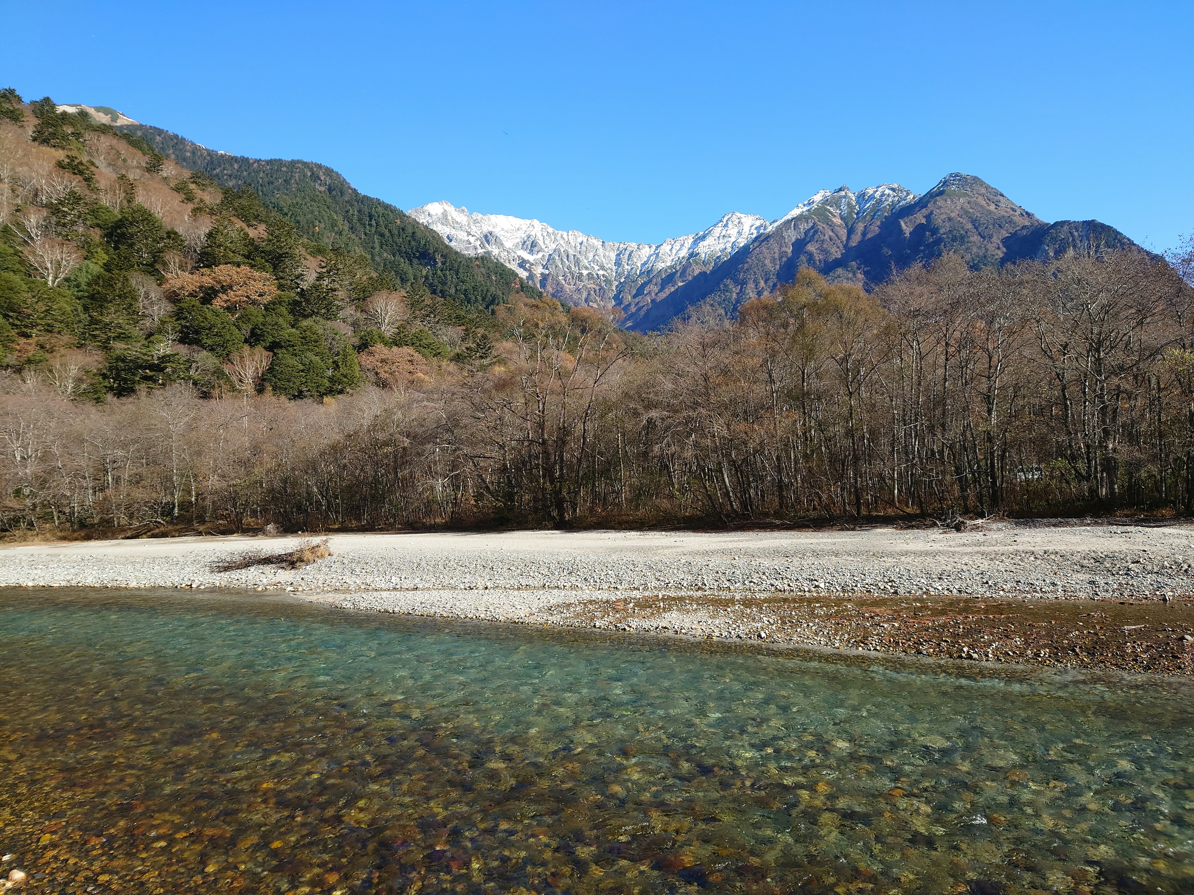 Vista escénica de un río claro bajo un cielo azul con montañas nevadas