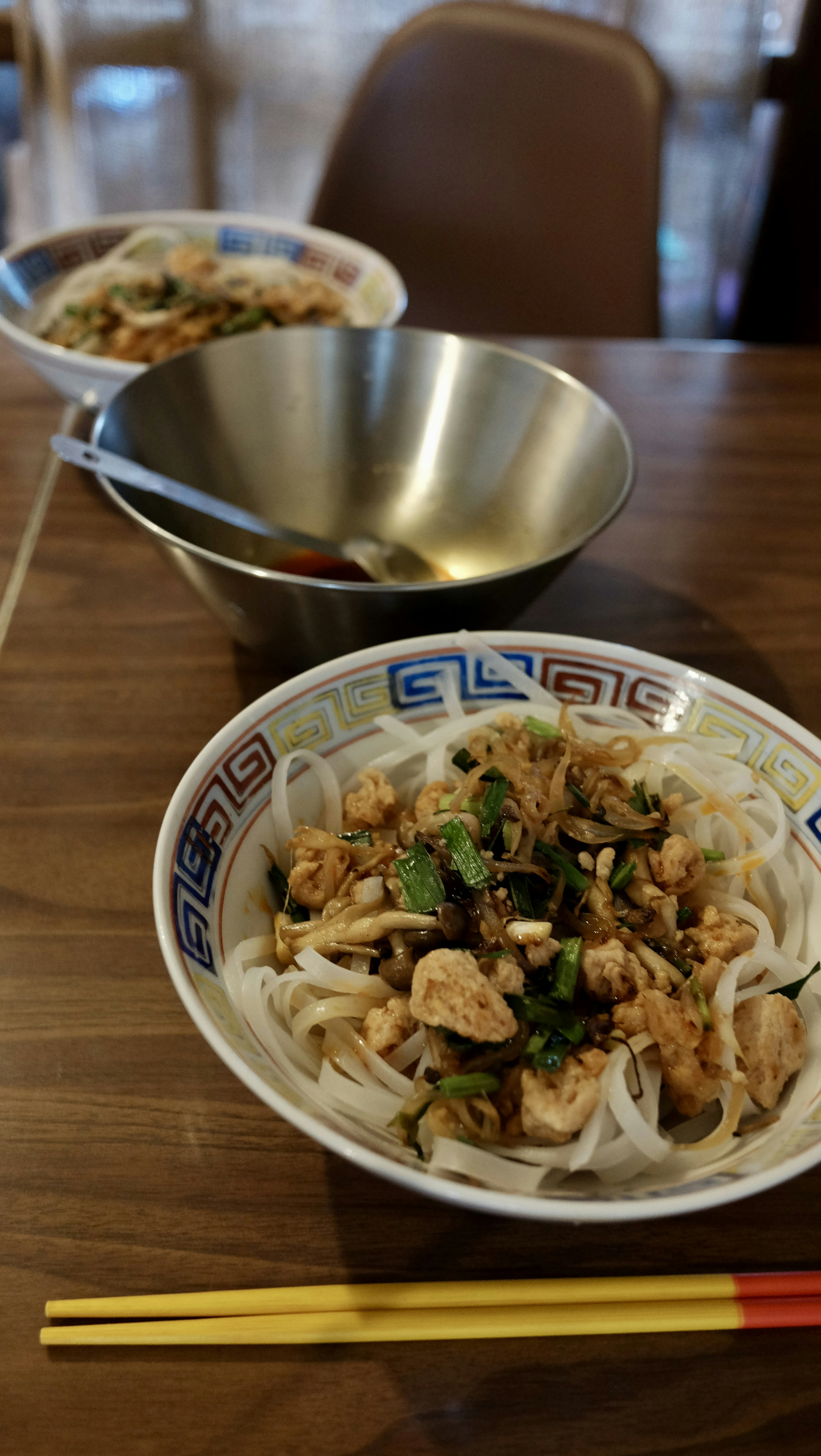 Bowl of chicken and vegetable pho on a table with a metal bowl in the background