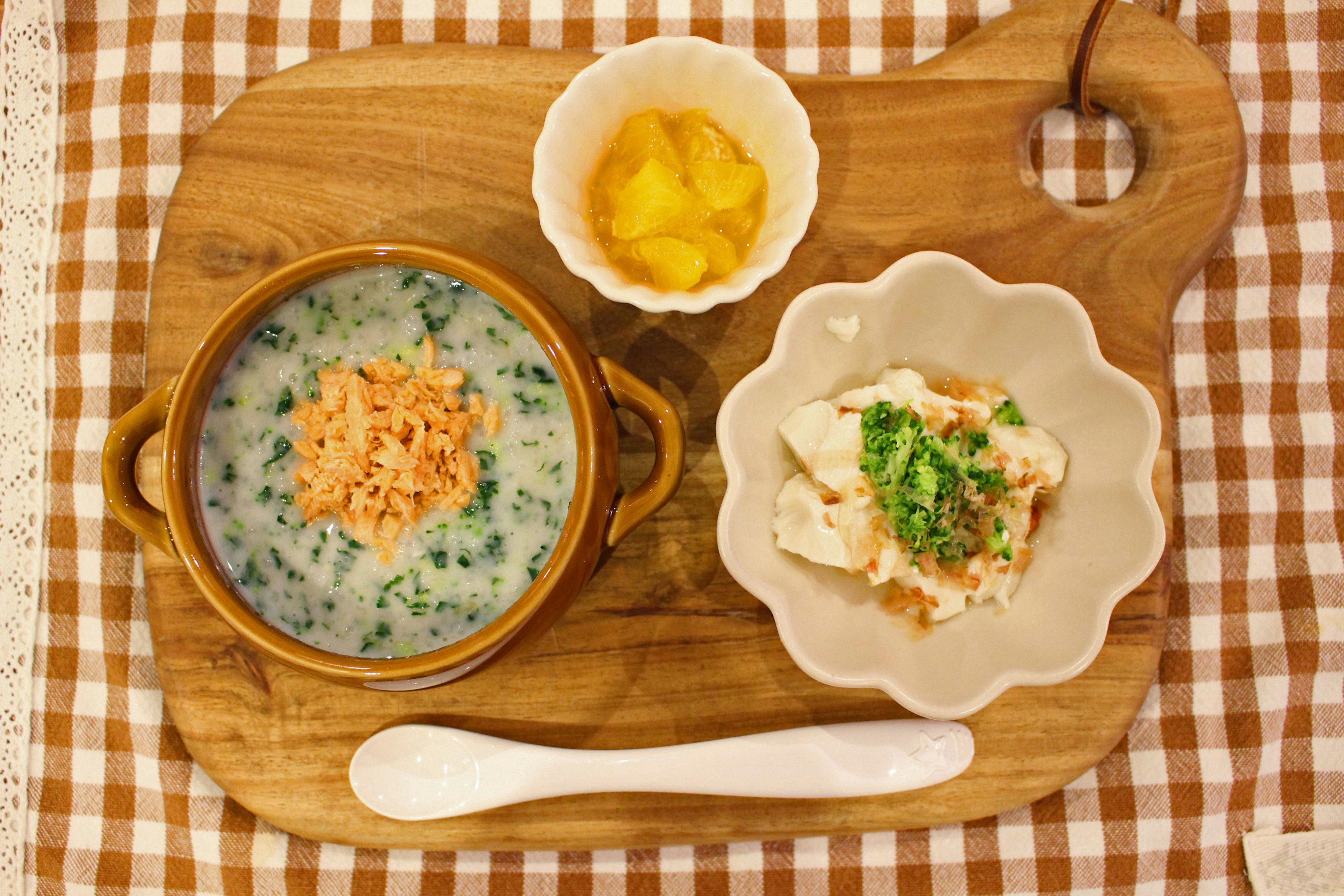 A wooden board featuring salmon porridge, tofu dish, and mango slices