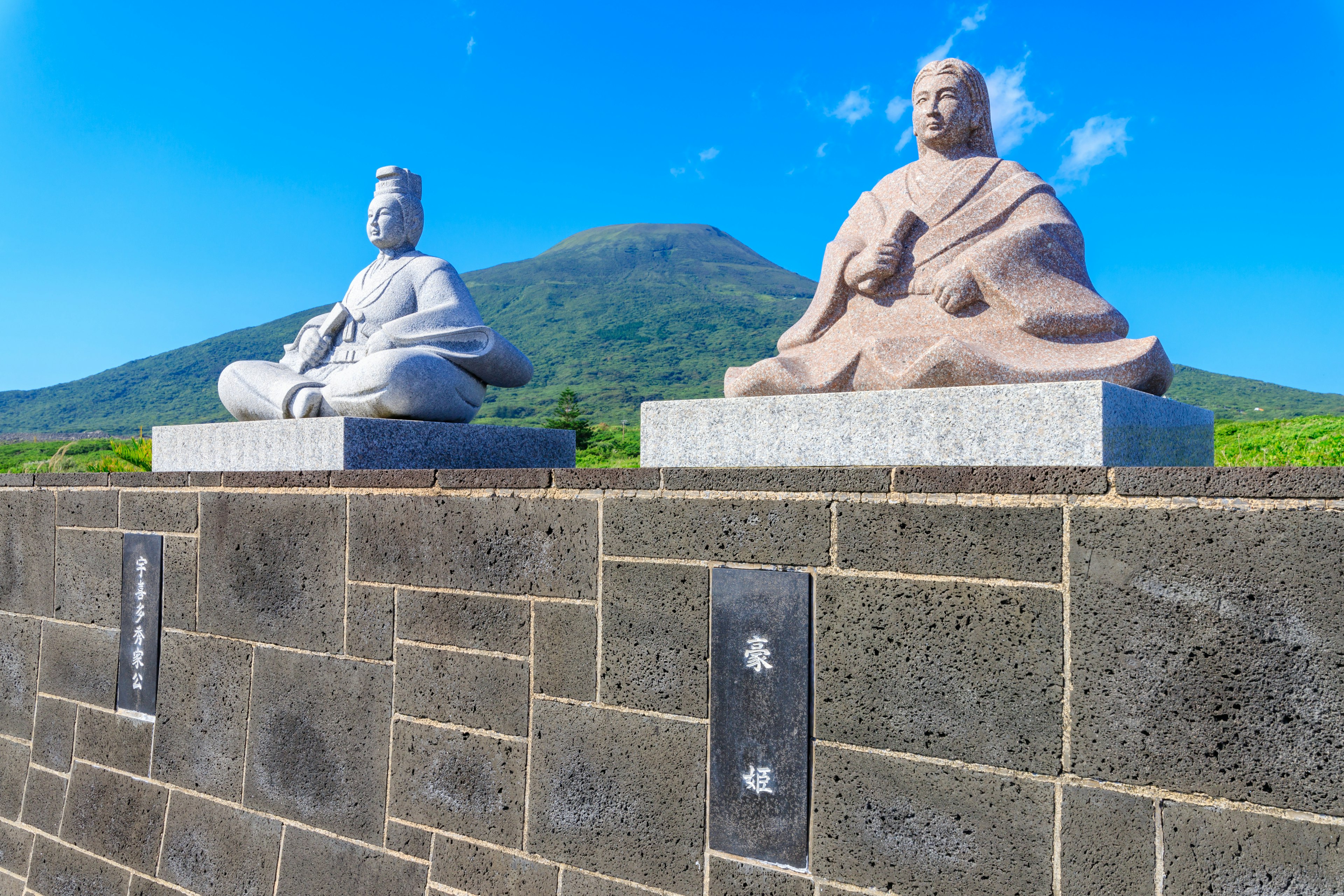 Two stone statues under a blue sky with a mountain in the background