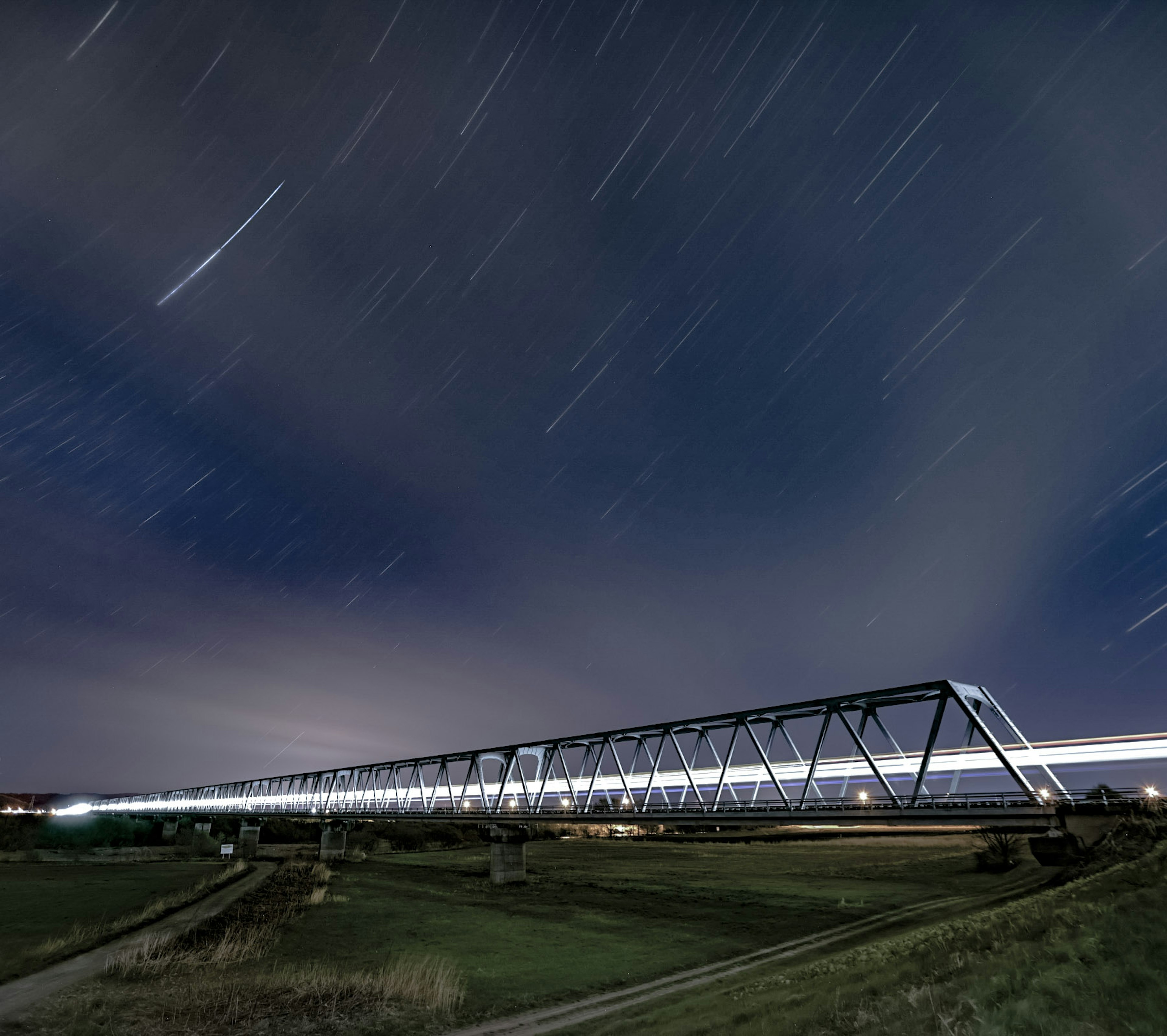 星の流れが見える夜空の下の鉄道橋の長時間露光写真