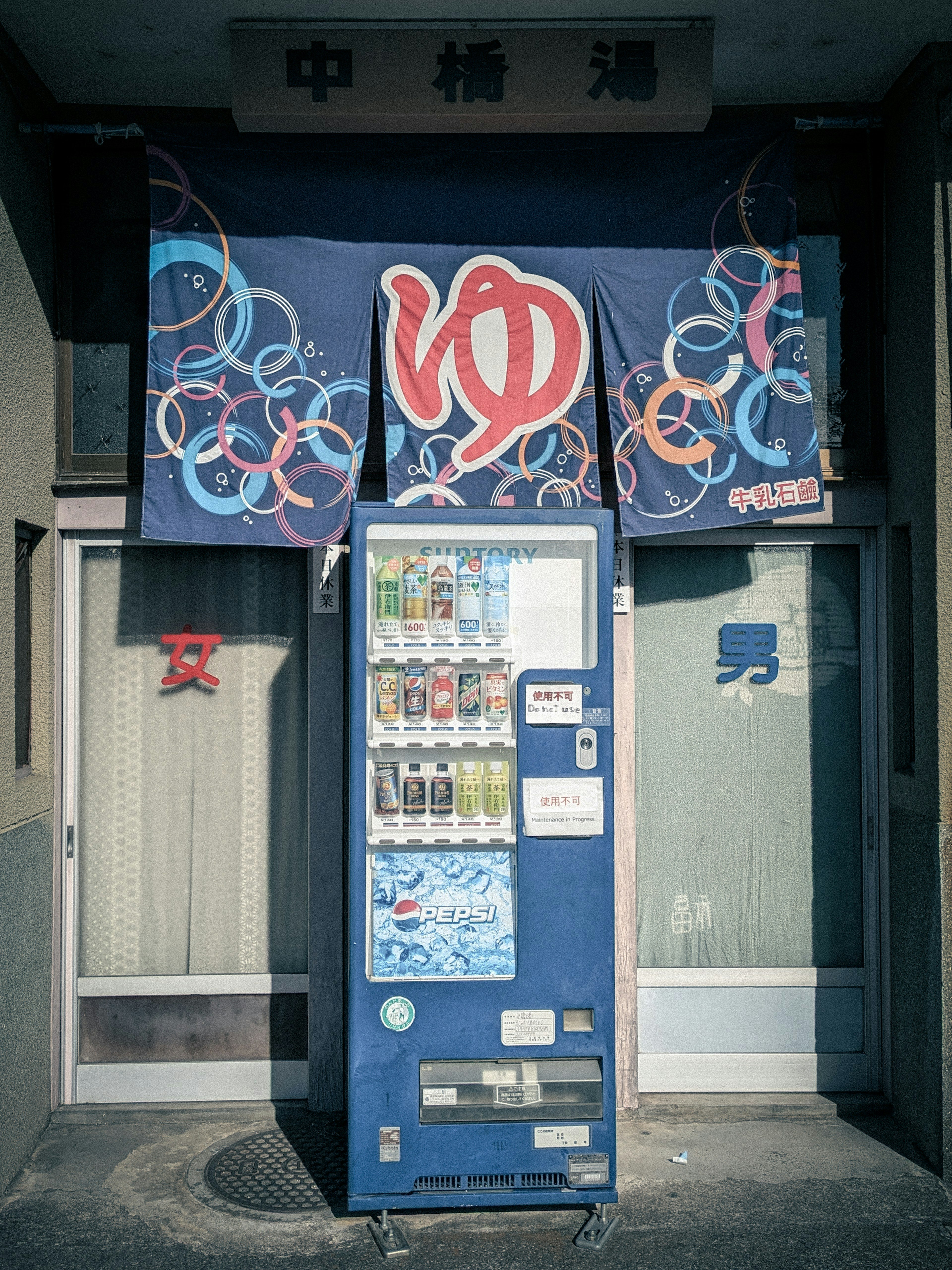 Distributeur automatique bleu devant un magasin avec un rideau noren japonais traditionnel