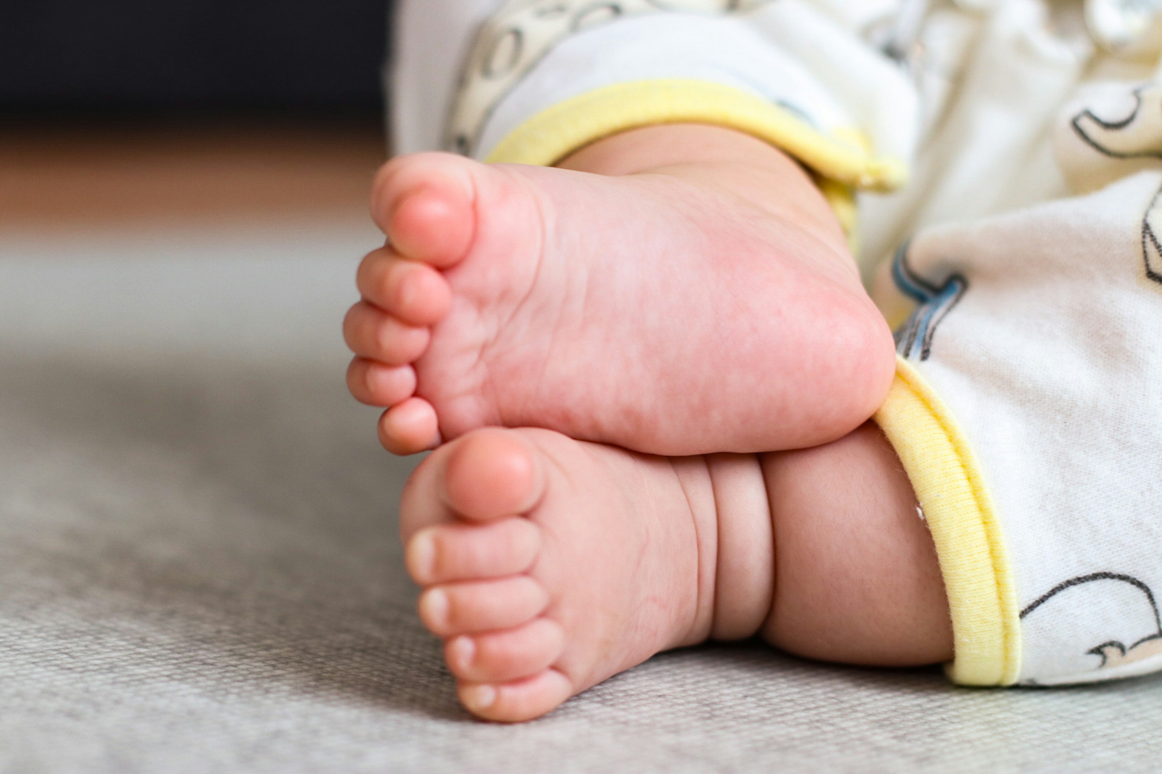 Close-up of a baby's feet overlapping soft skin tone and yellow pajama cuffs