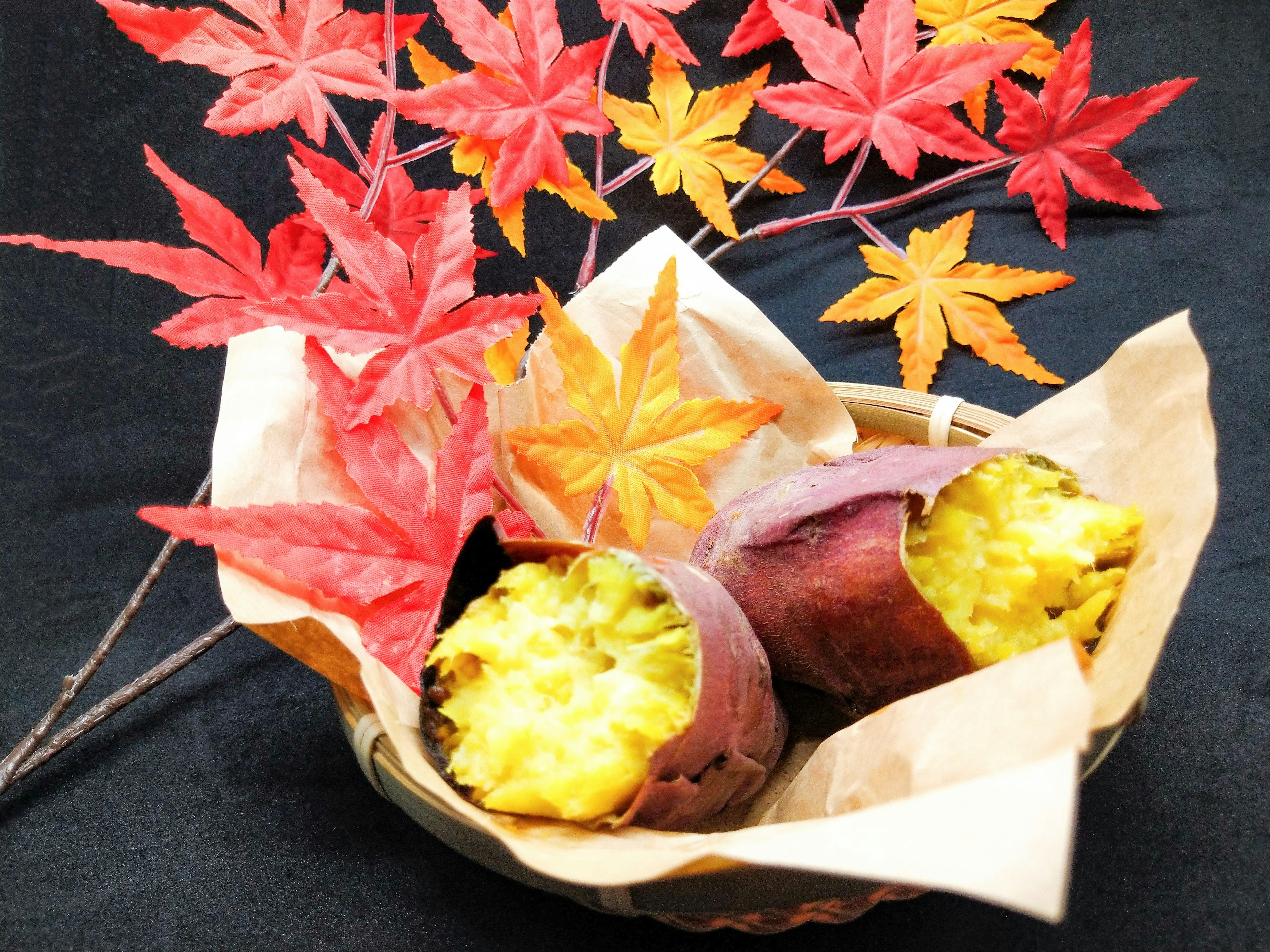 A basket containing roasted sweet potatoes and autumn maple leaves