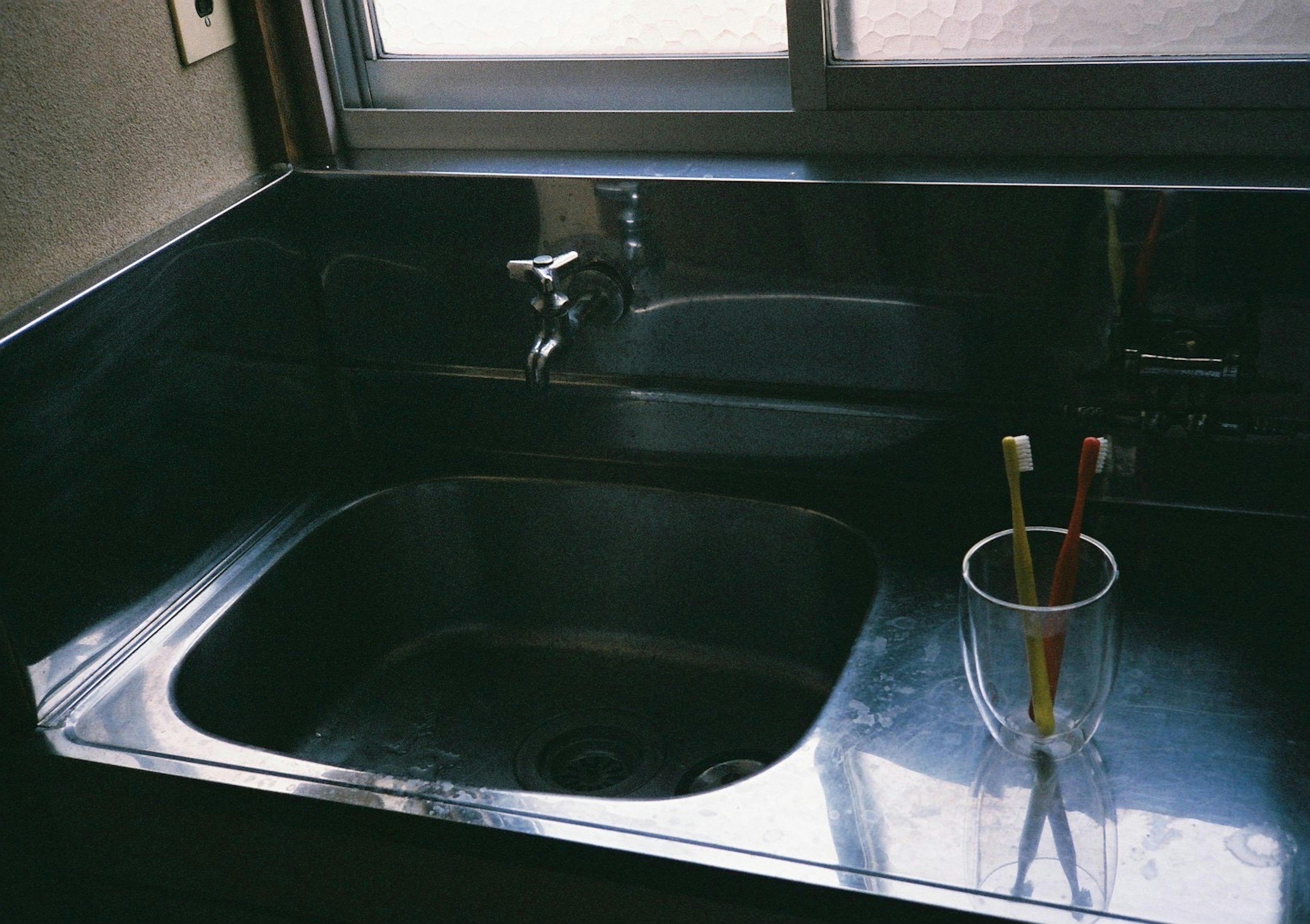 Évier de cuisine simple avec des brosses à dents dans une tasse et une fenêtre