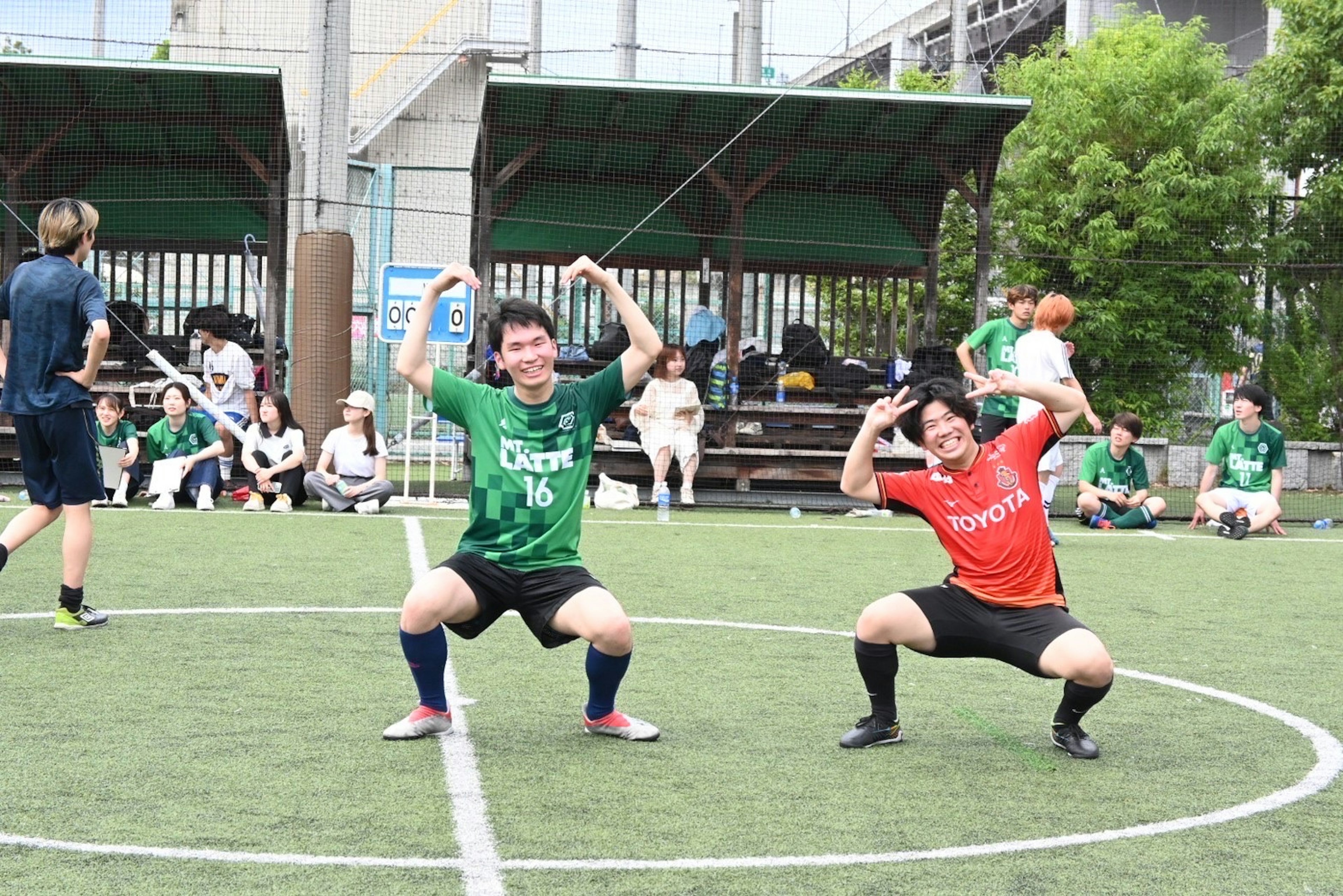 Two men posing on a soccer field One wears a green uniform and the other wears a red uniform