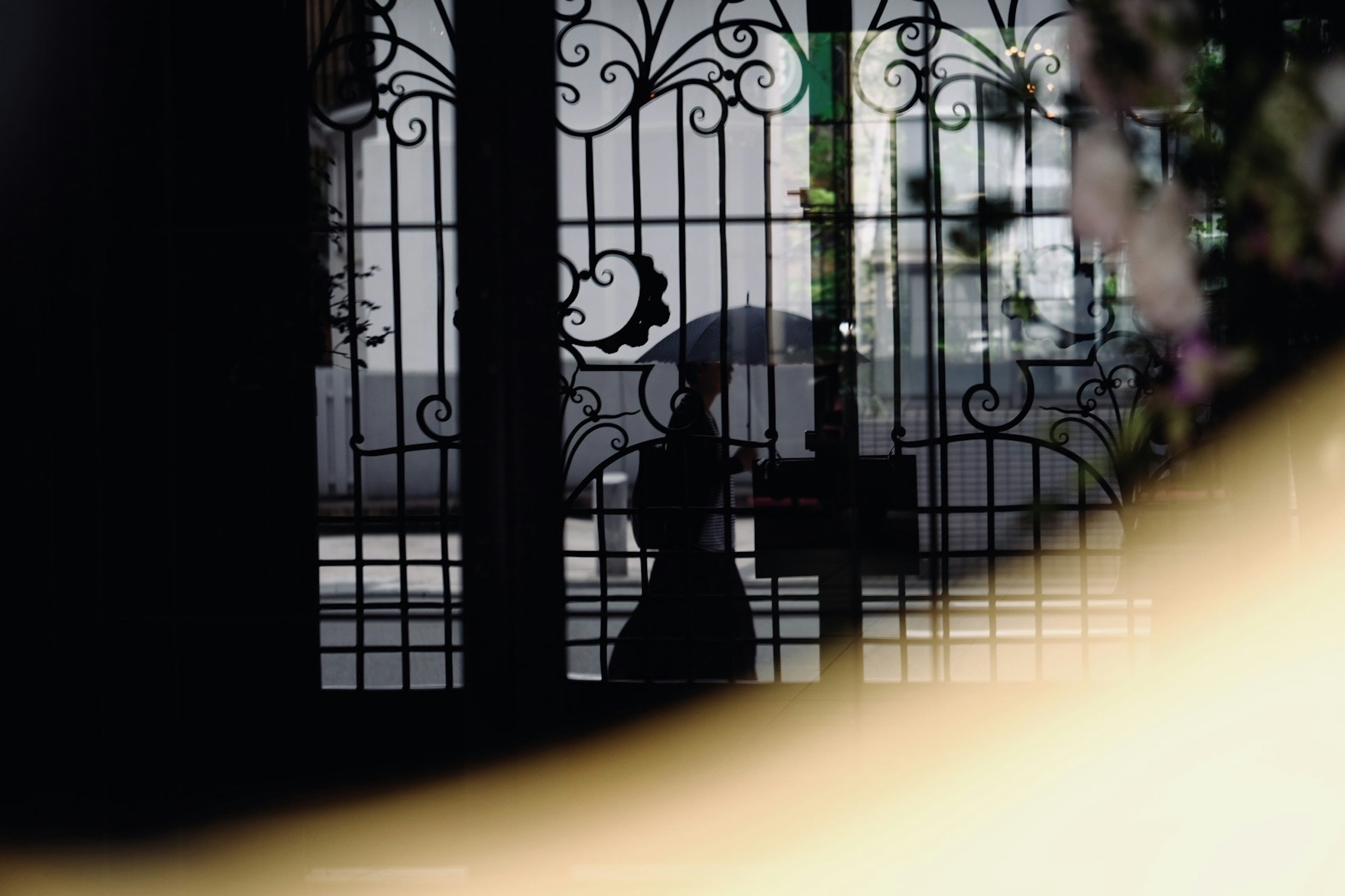 Silhouette d'une personne tenant un parapluie derrière des grilles ornées