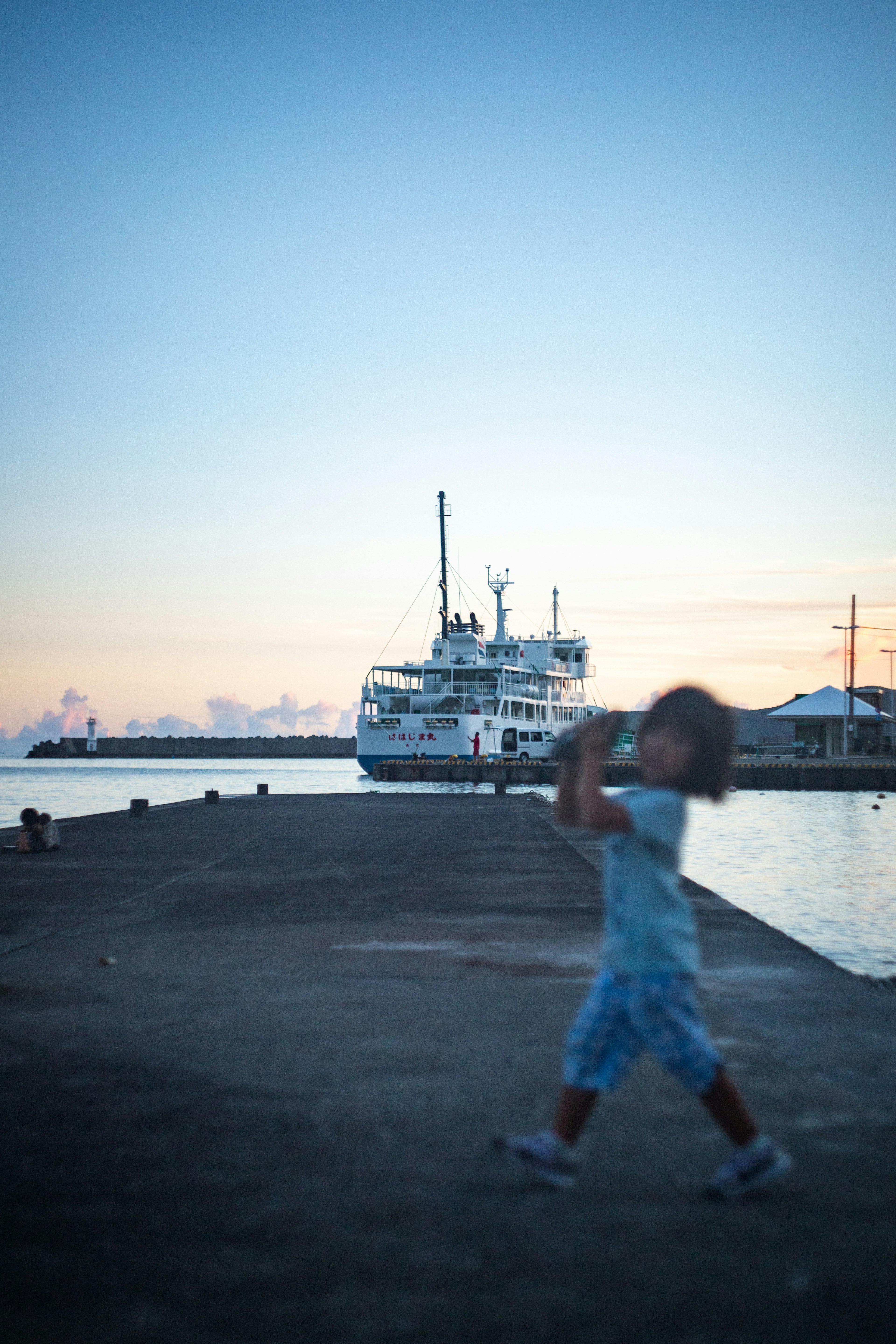 Child playing at the harbor during sunset with a ship in the background