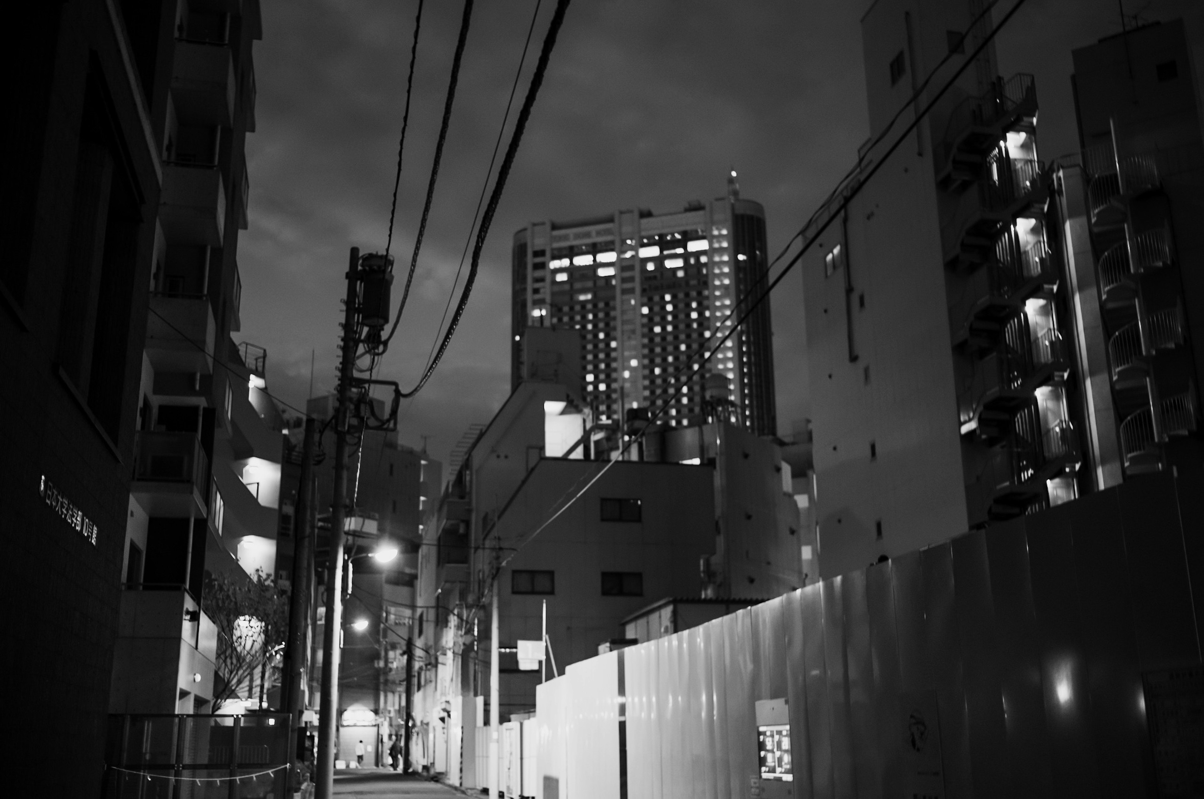 Black and white photo of a tall building at night surrounded by smaller structures