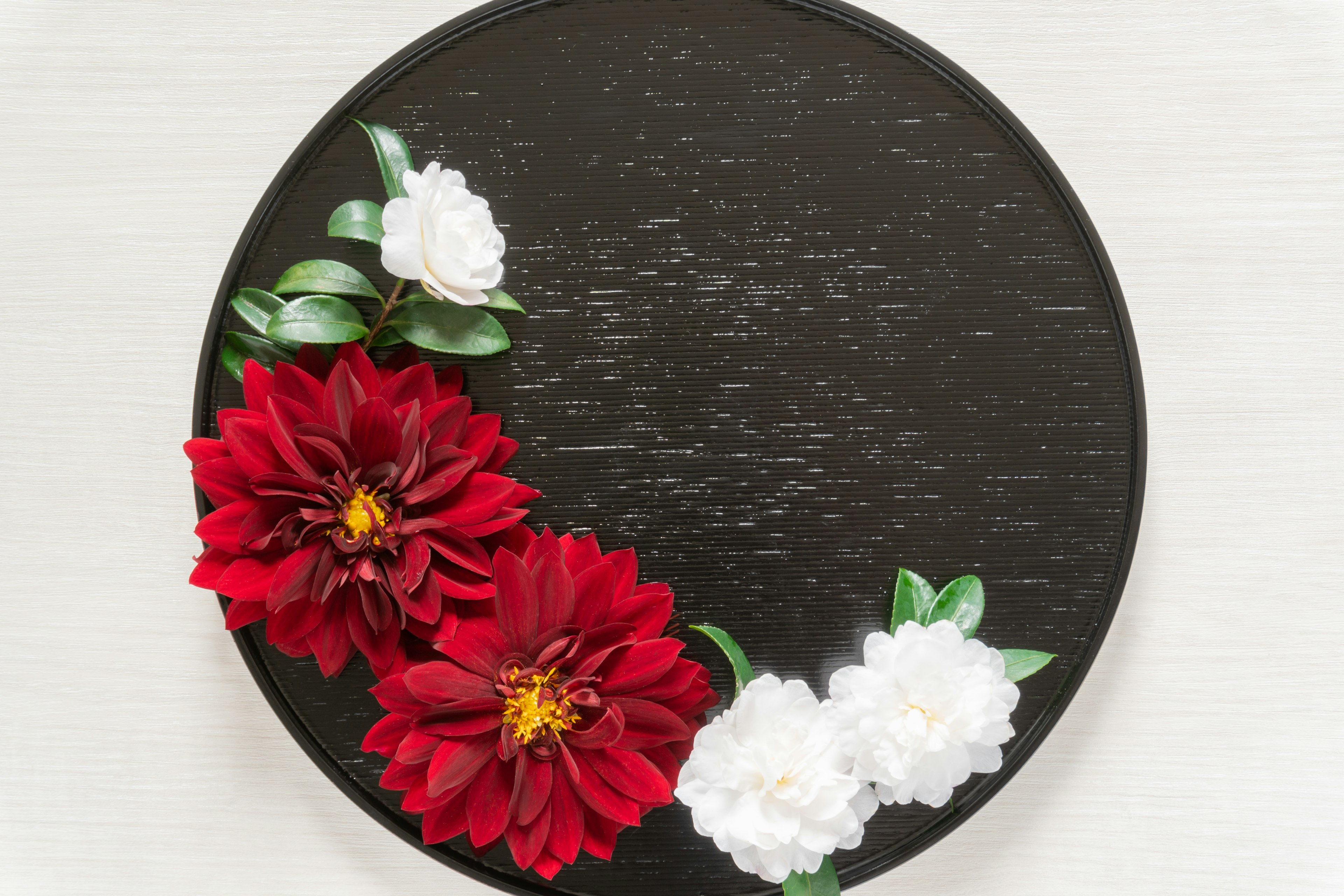 A round black tray featuring red dahlias and white flowers arranged decoratively