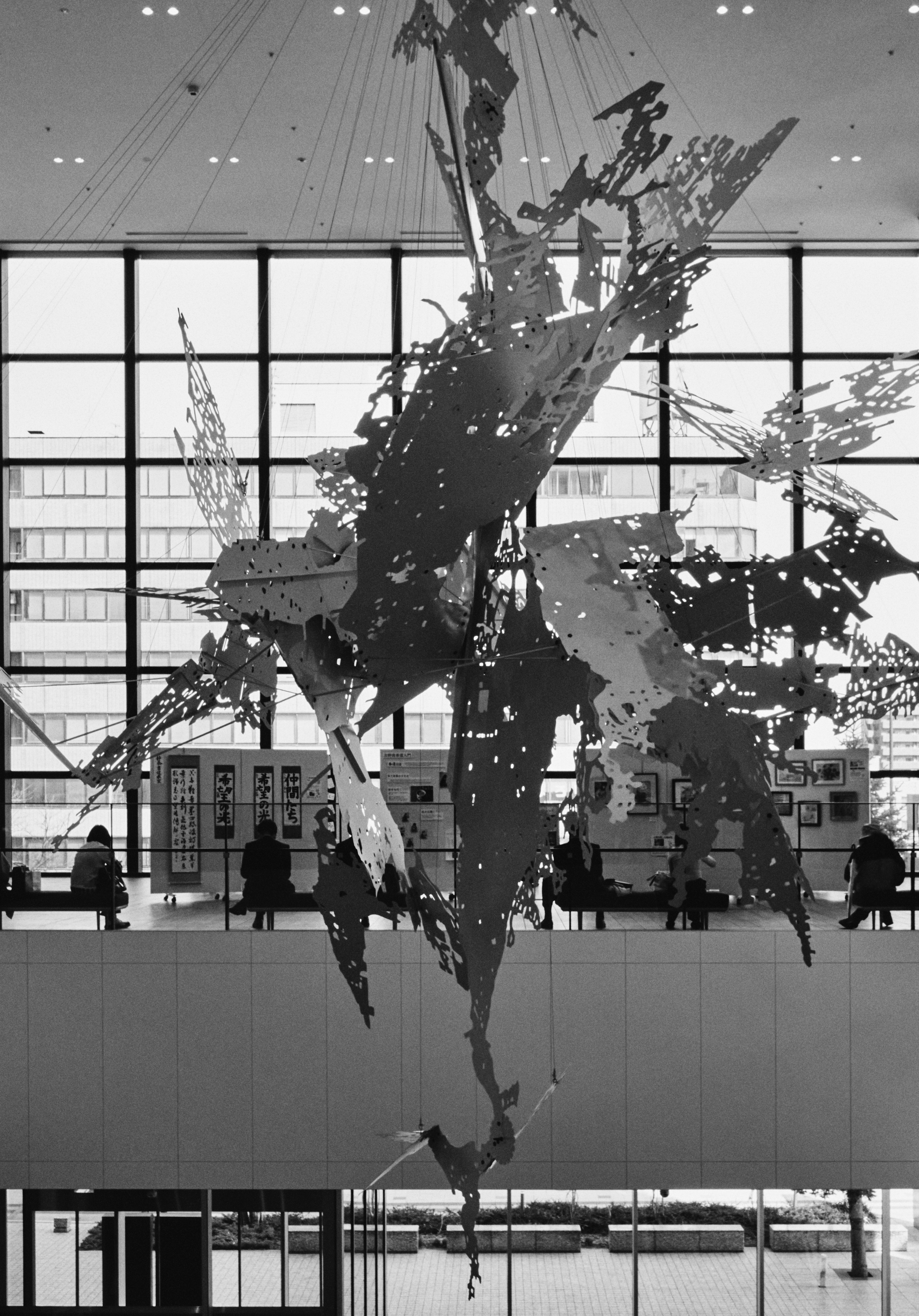 Instalación artística abstracta en blanco y negro suspendida cerca de grandes ventanas con personas visibles en el espacio