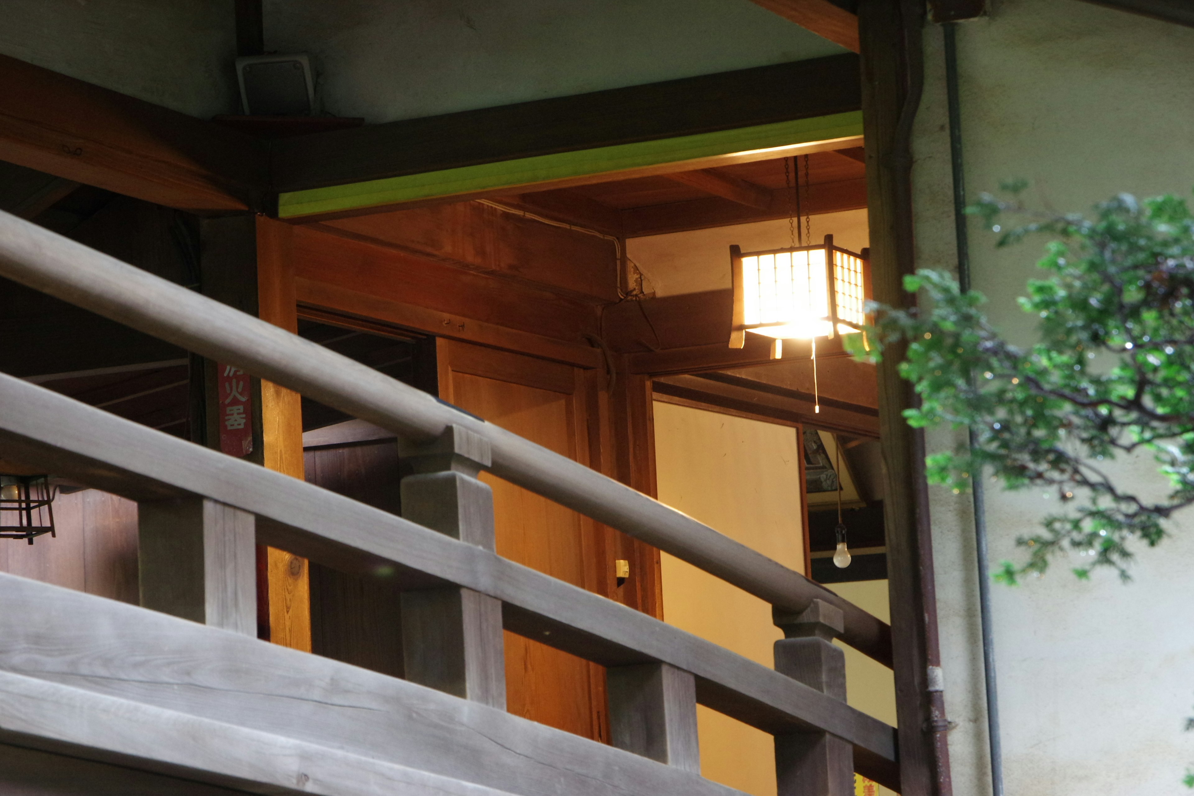 Part of a traditional Japanese building with wooden railing and a soft lantern light