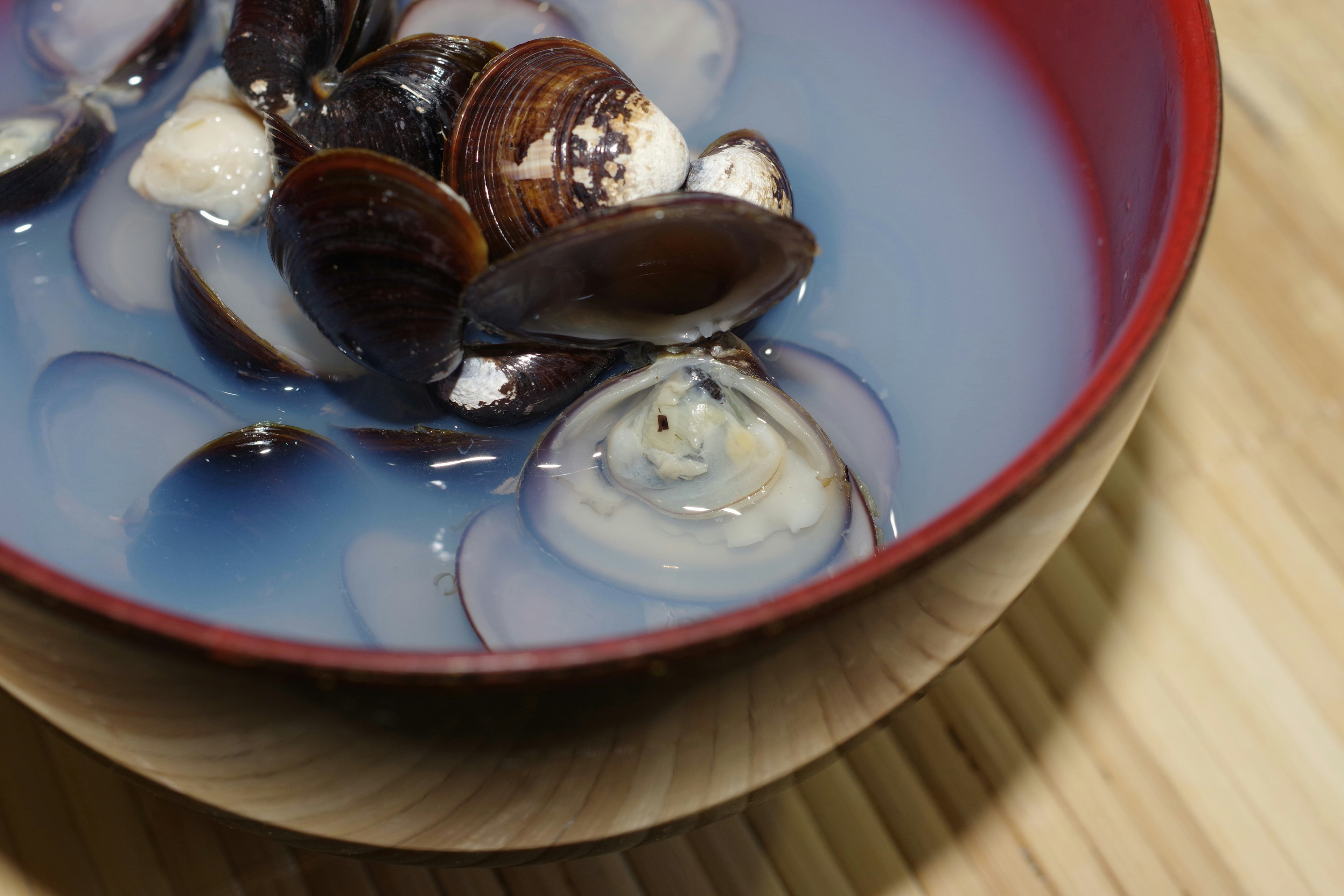 A red bowl filled with clam soup featuring various clams in a blue broth