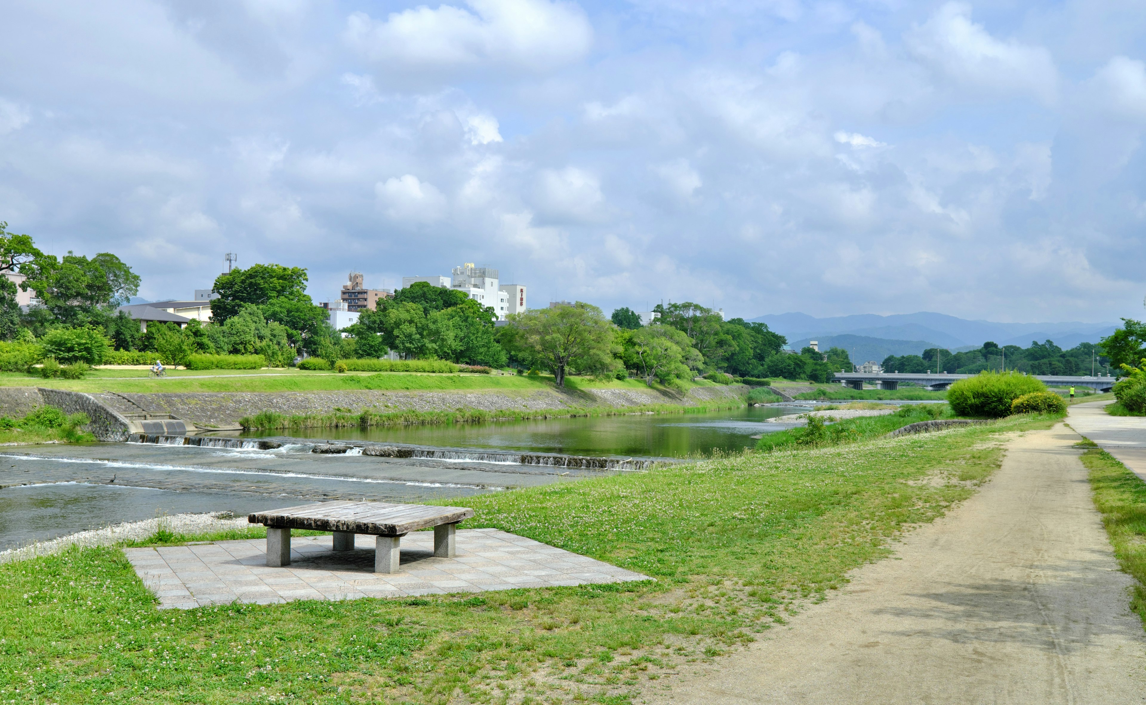 Vista escénica de un parque verde junto a un río con un banco y un sendero