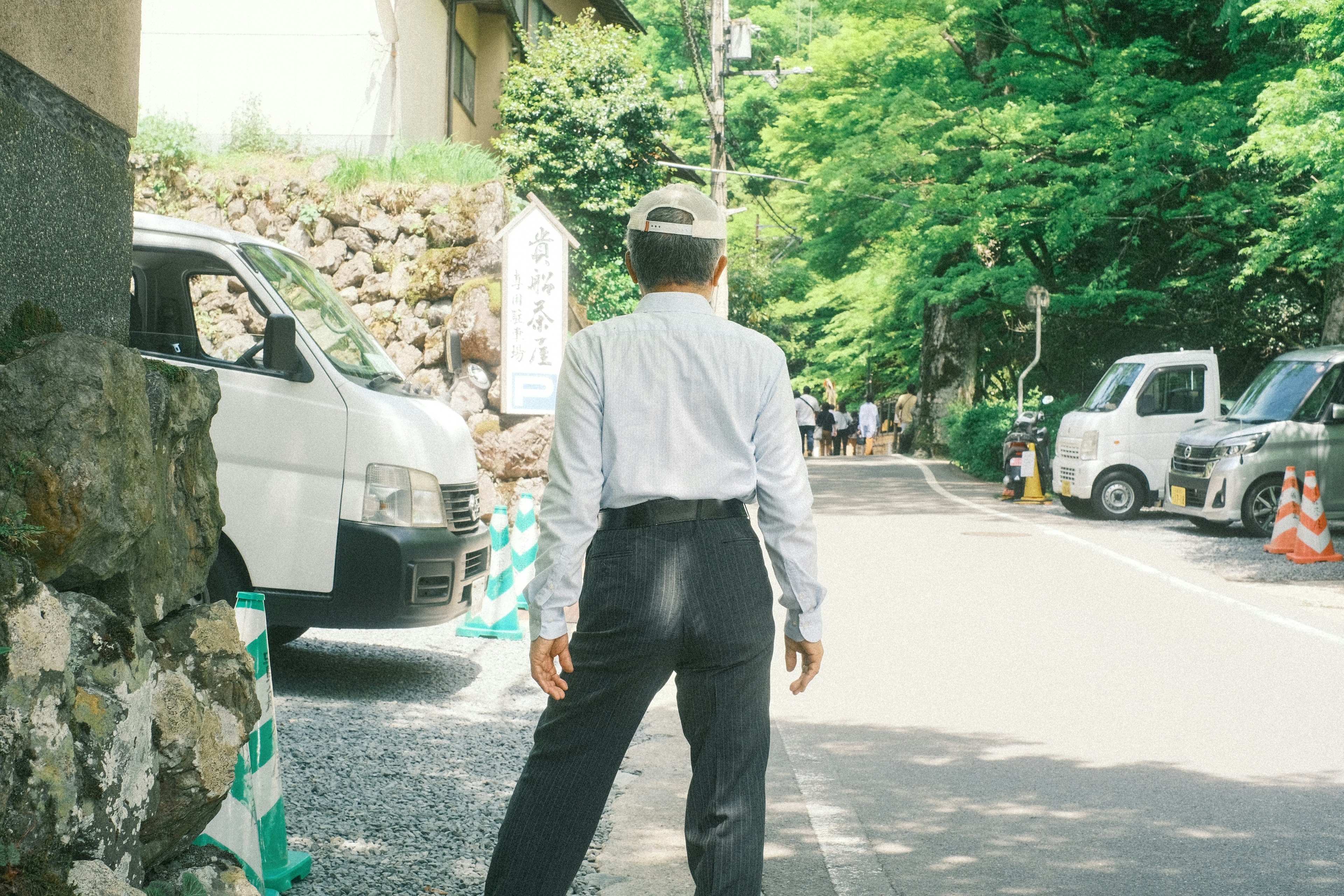 Man in white shirt and black pants standing on a quiet street surrounded by green trees