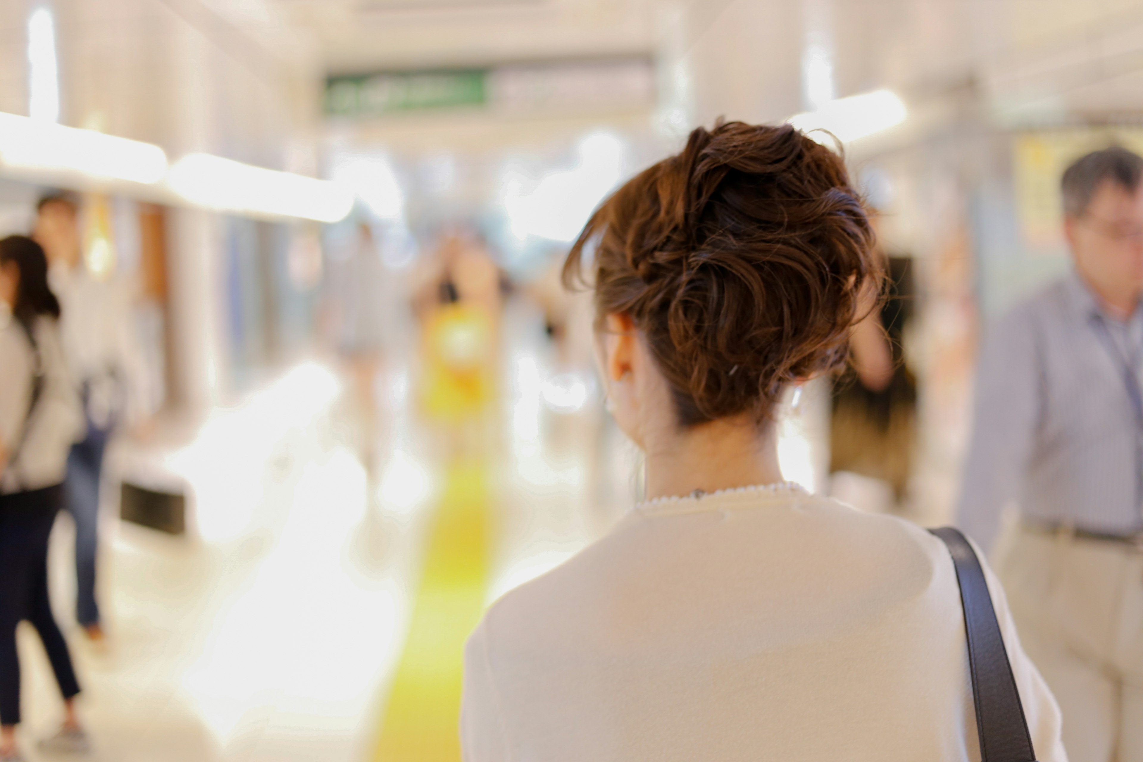 Una donna che cammina in un corridoio luminoso con figure sfocate sullo sfondo