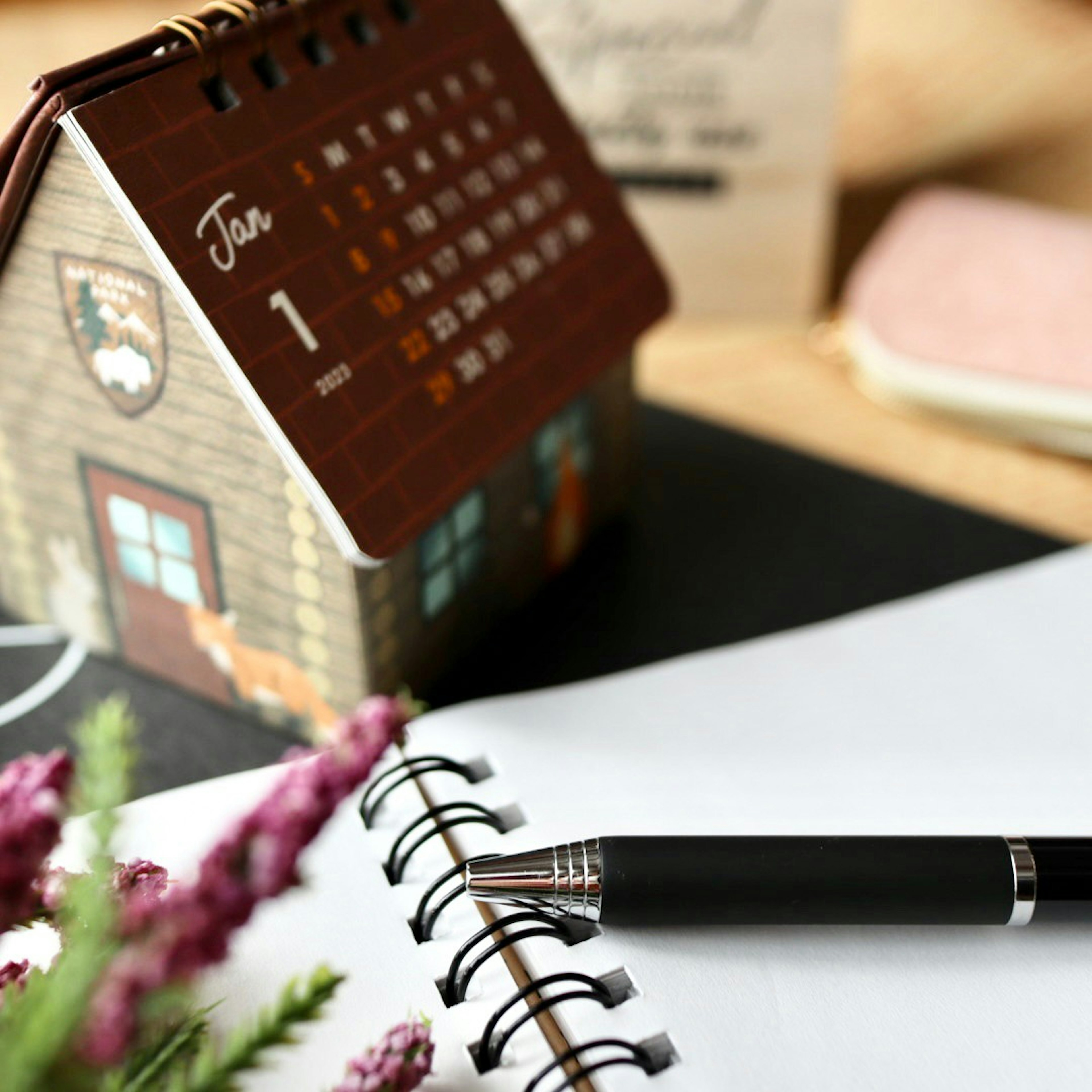 A desk scene featuring a house-shaped calendar a notebook and a pen