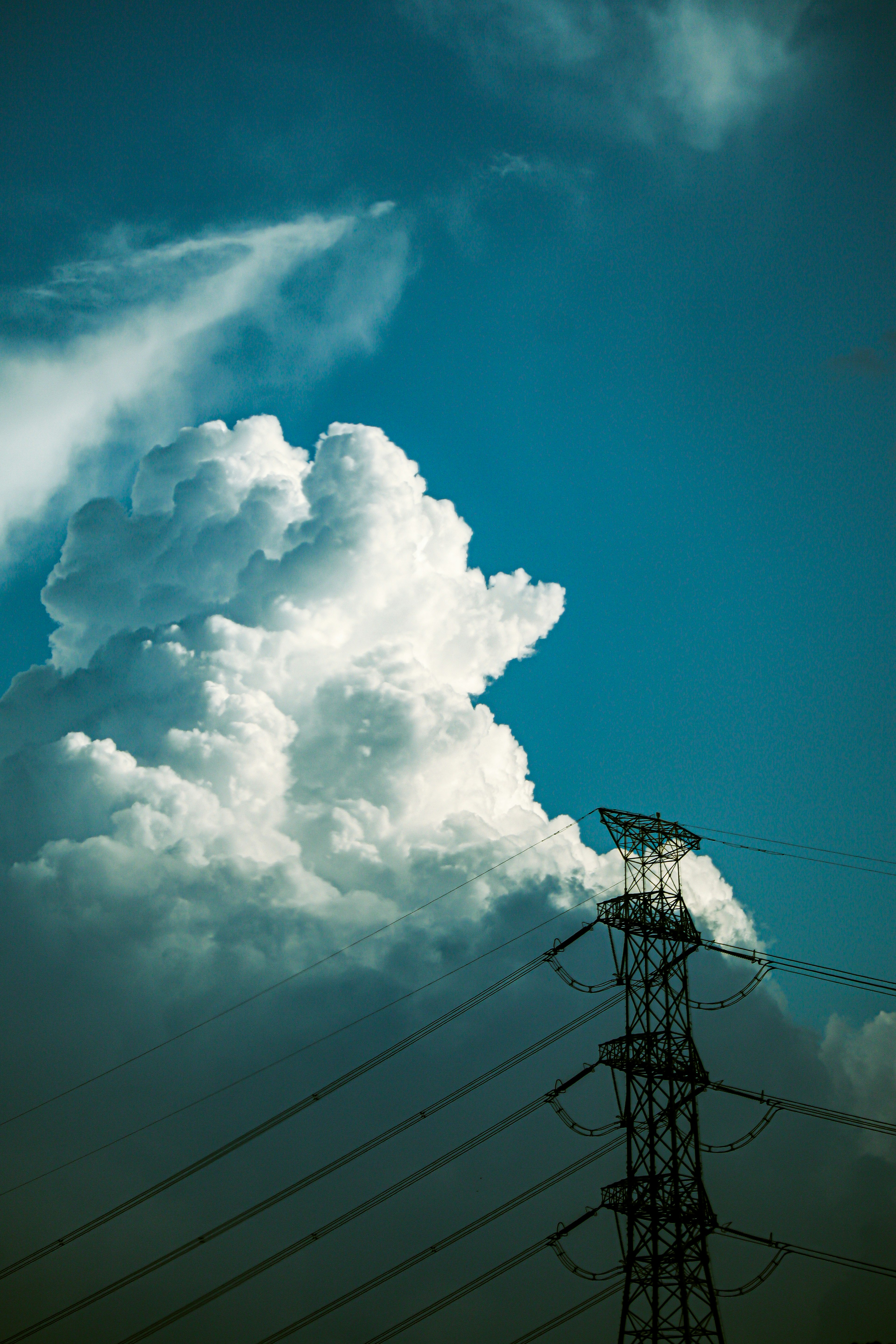 Power lines silhouetted against a blue sky with fluffy white clouds