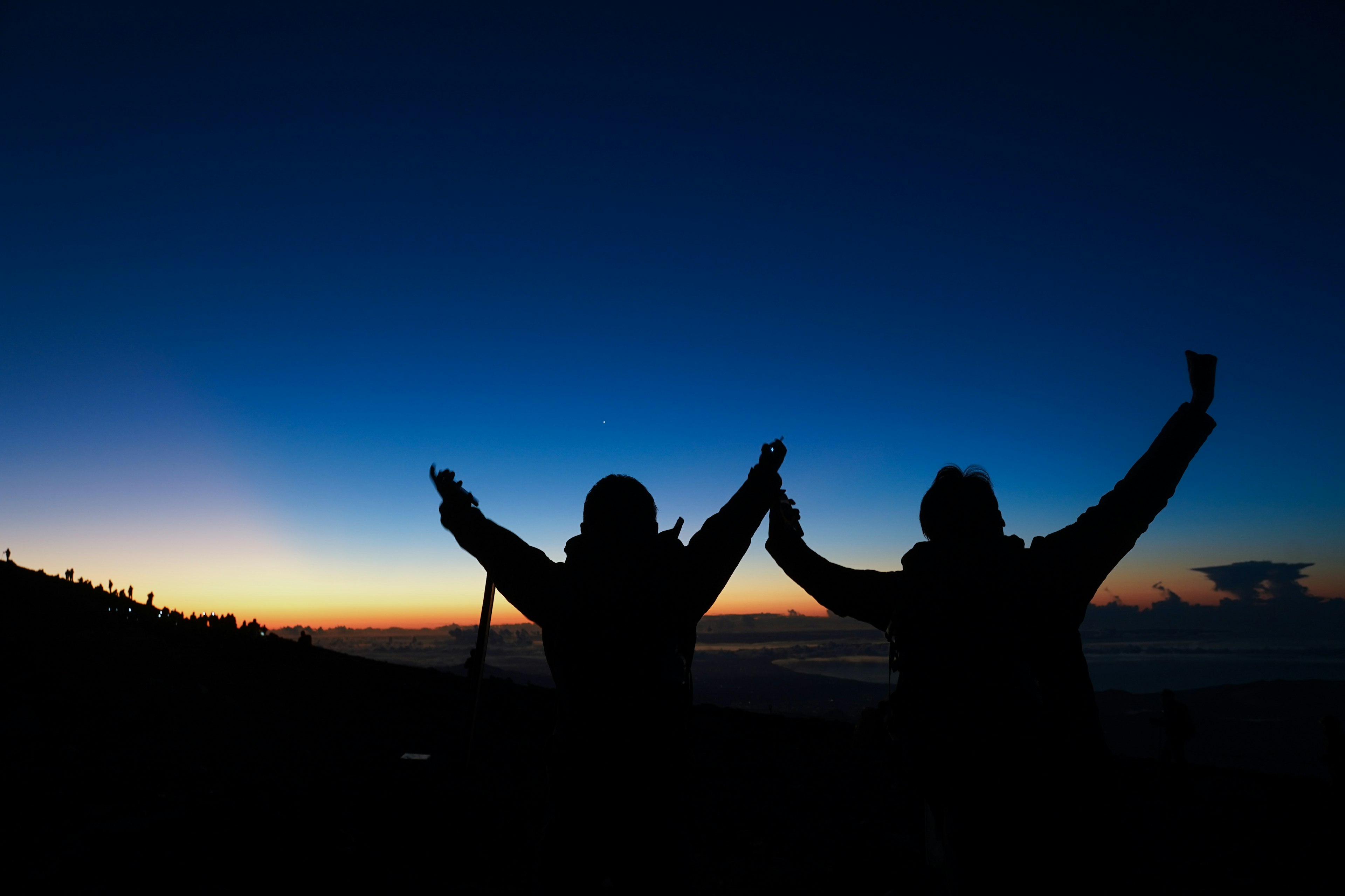 二人のシルエットが夕焼けを背景に手を挙げている