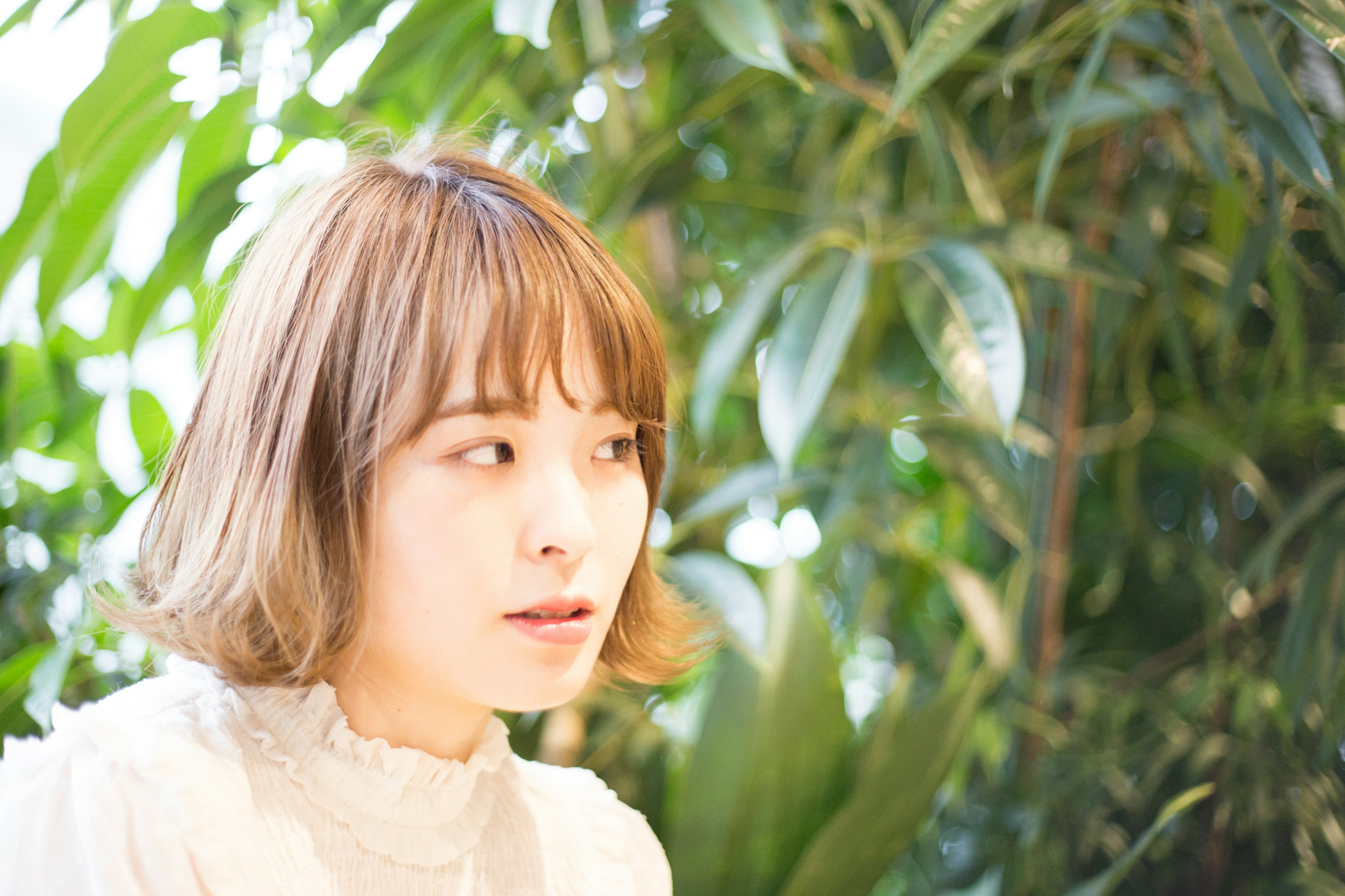 Portrait d'une femme assise devant des plantes vertes avec des cheveux clairs et une expression douce