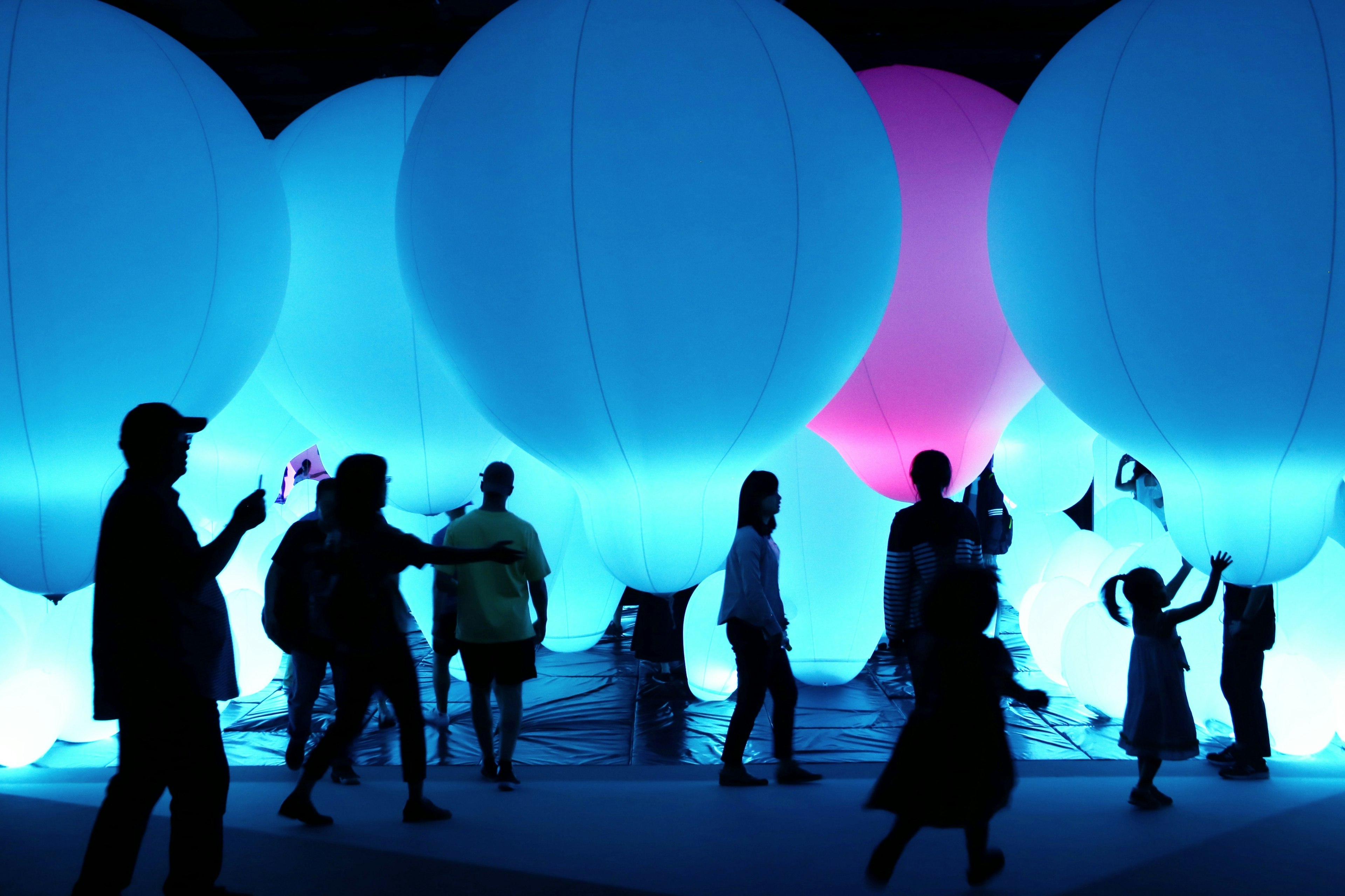 Silhouetten von Menschen, die sich um große Ballons in Blau- und Rosatönen versammeln