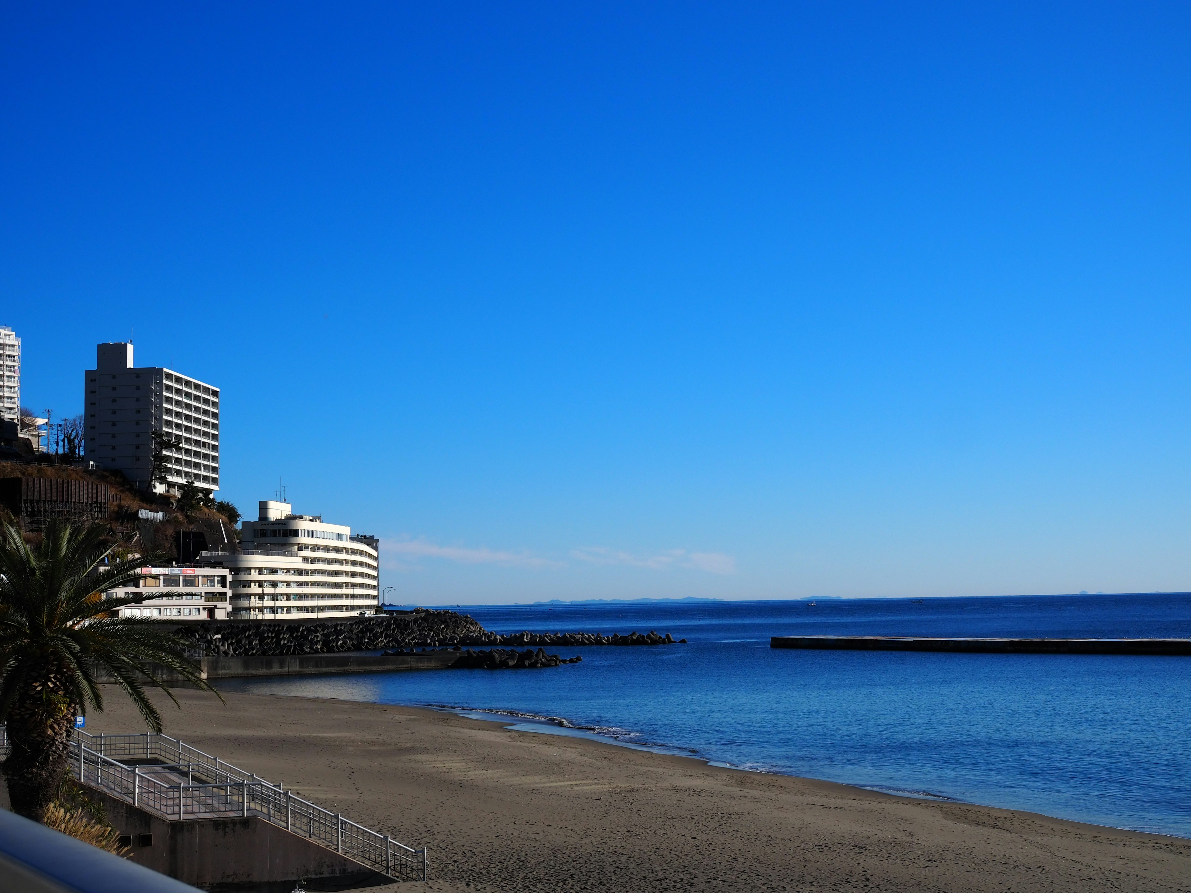 Strandansicht mit blauem Himmel und ruhiger See mit Hochhäusern und Palmen