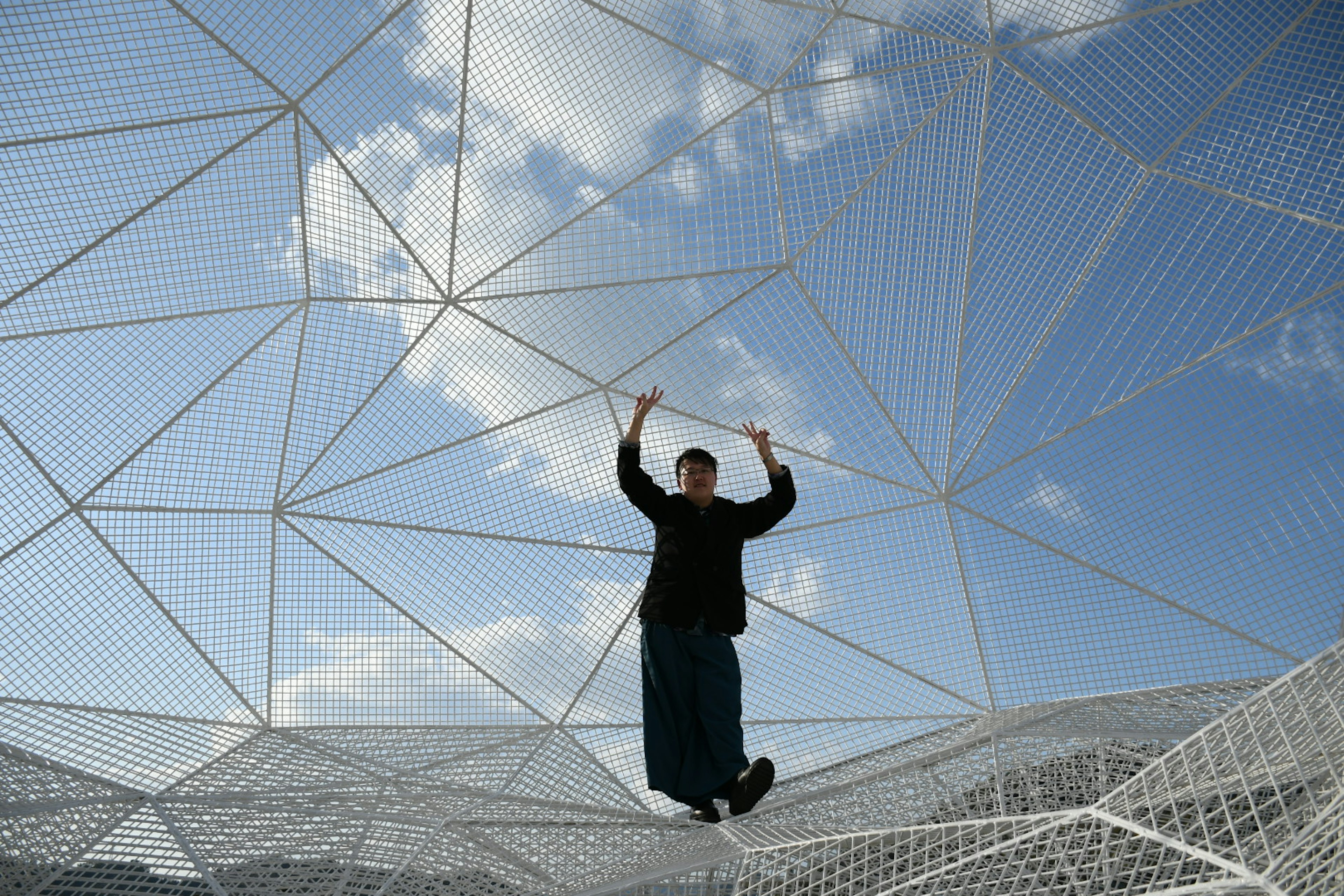 Man balancing inside a white mesh structure under a blue sky