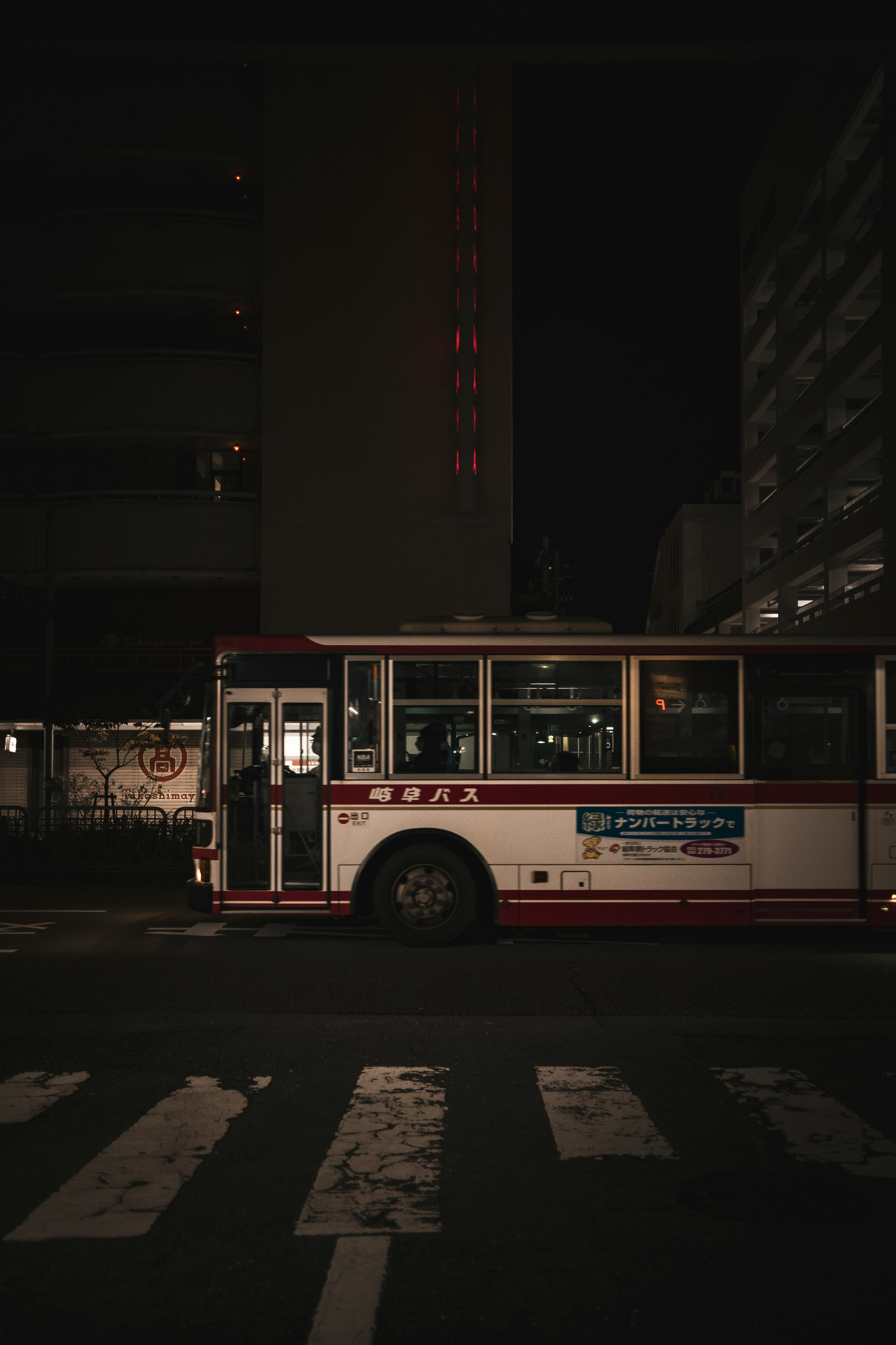 A bus parked at a street corner at night featuring a red and white design